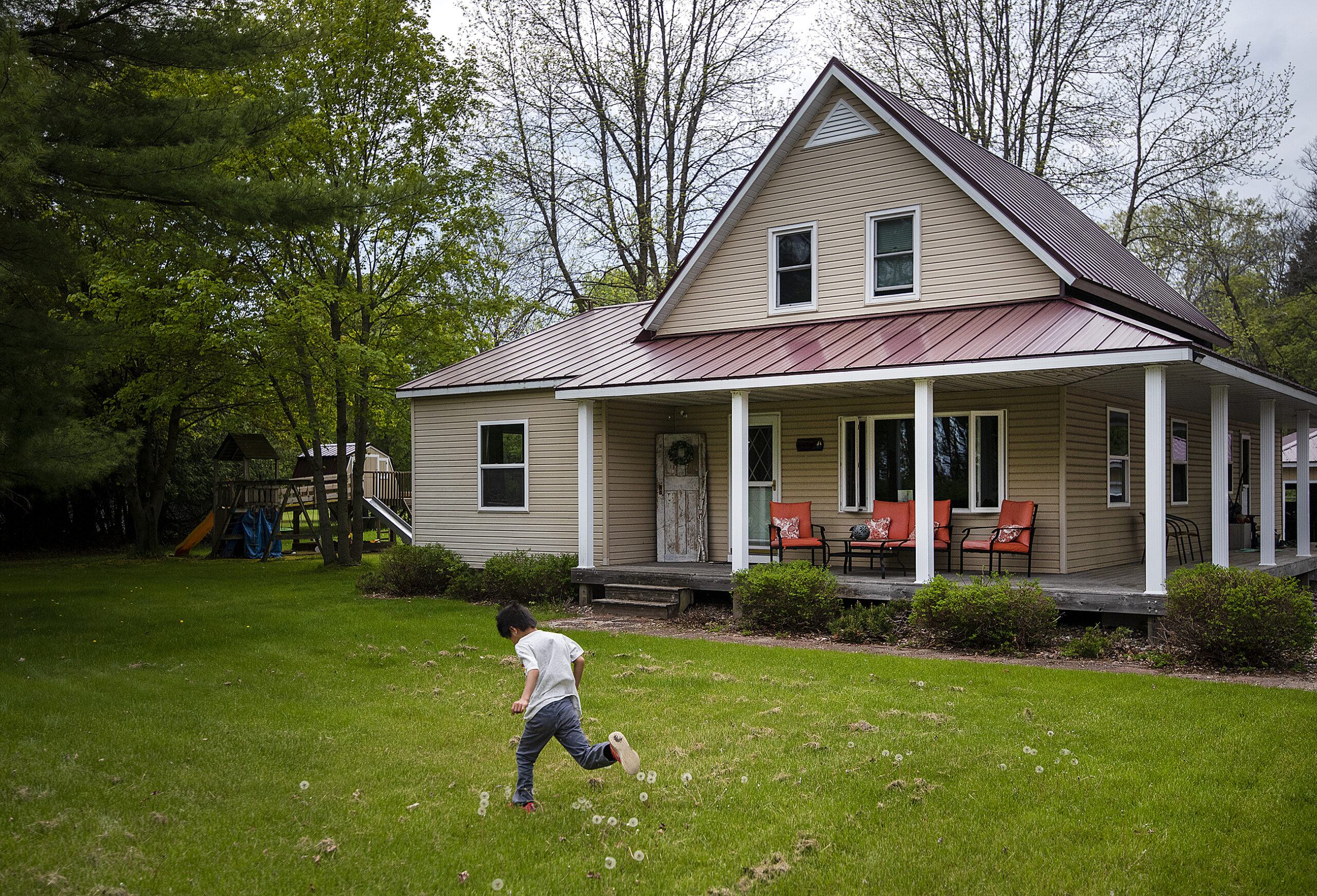 A child runs across a green lawn in front of a home with a wrap-around porch.