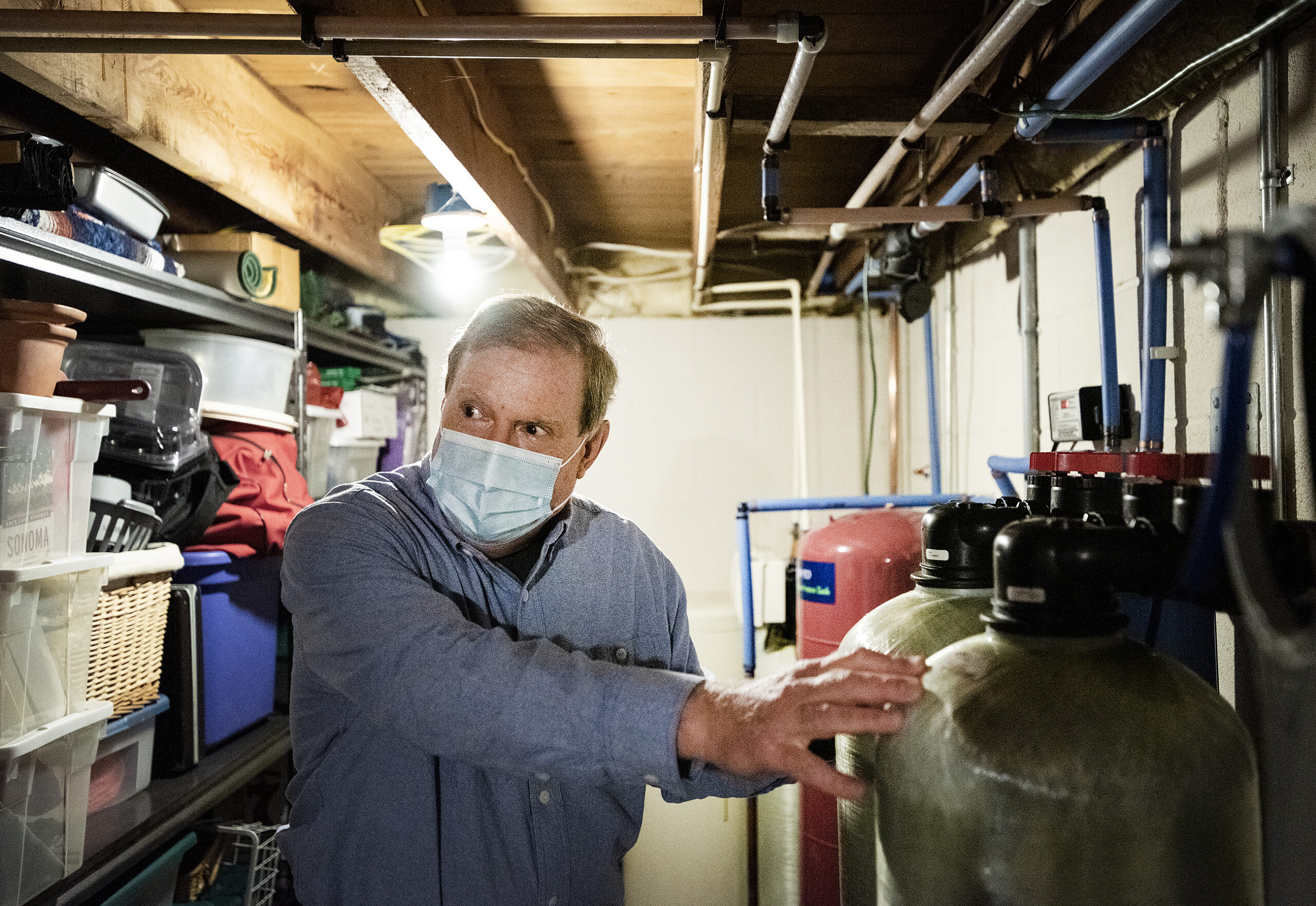 A man puts his hand on a water filter in his basement.