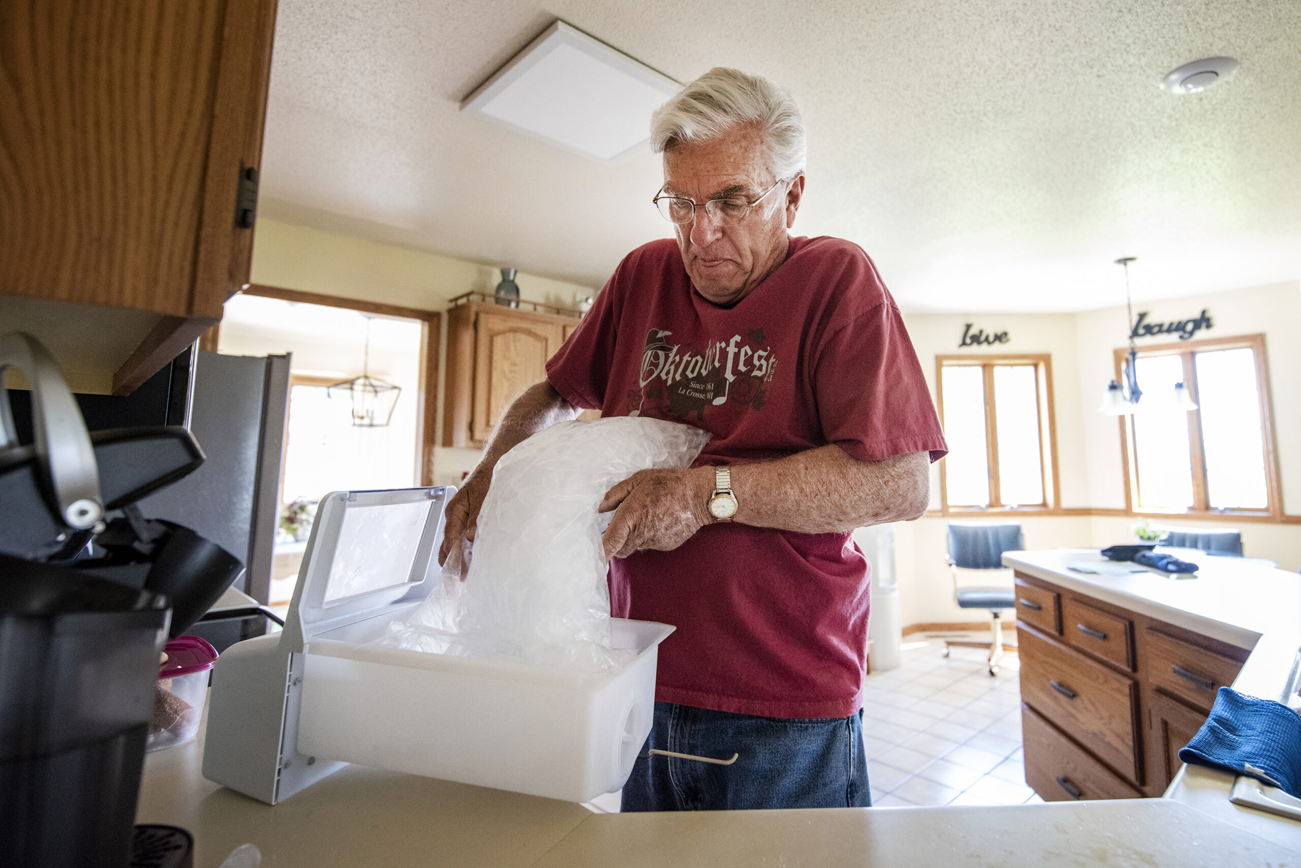 A man dumps a clear plastic bag of ice into a white box in a kitchen.