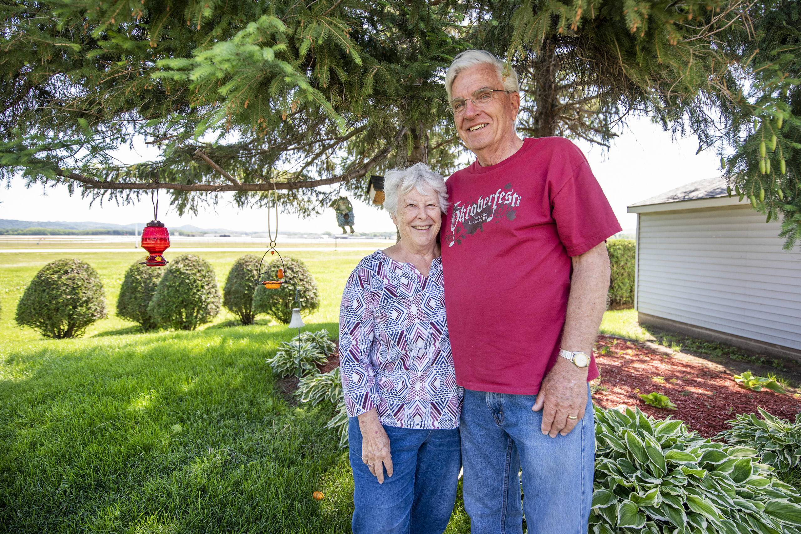 Two people stand under a tree in their yard.