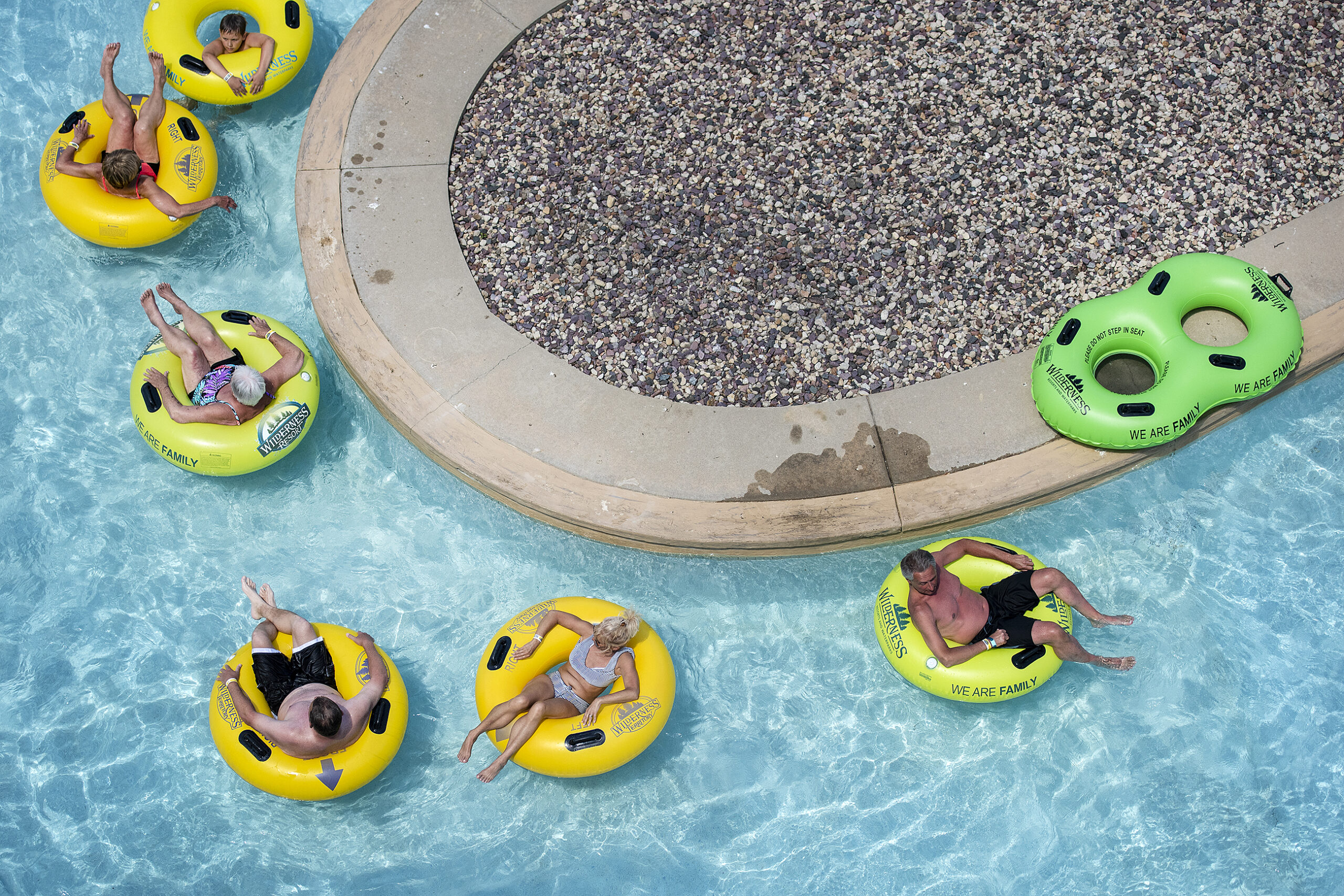People float in light blue water in yellow and green inner tubes.