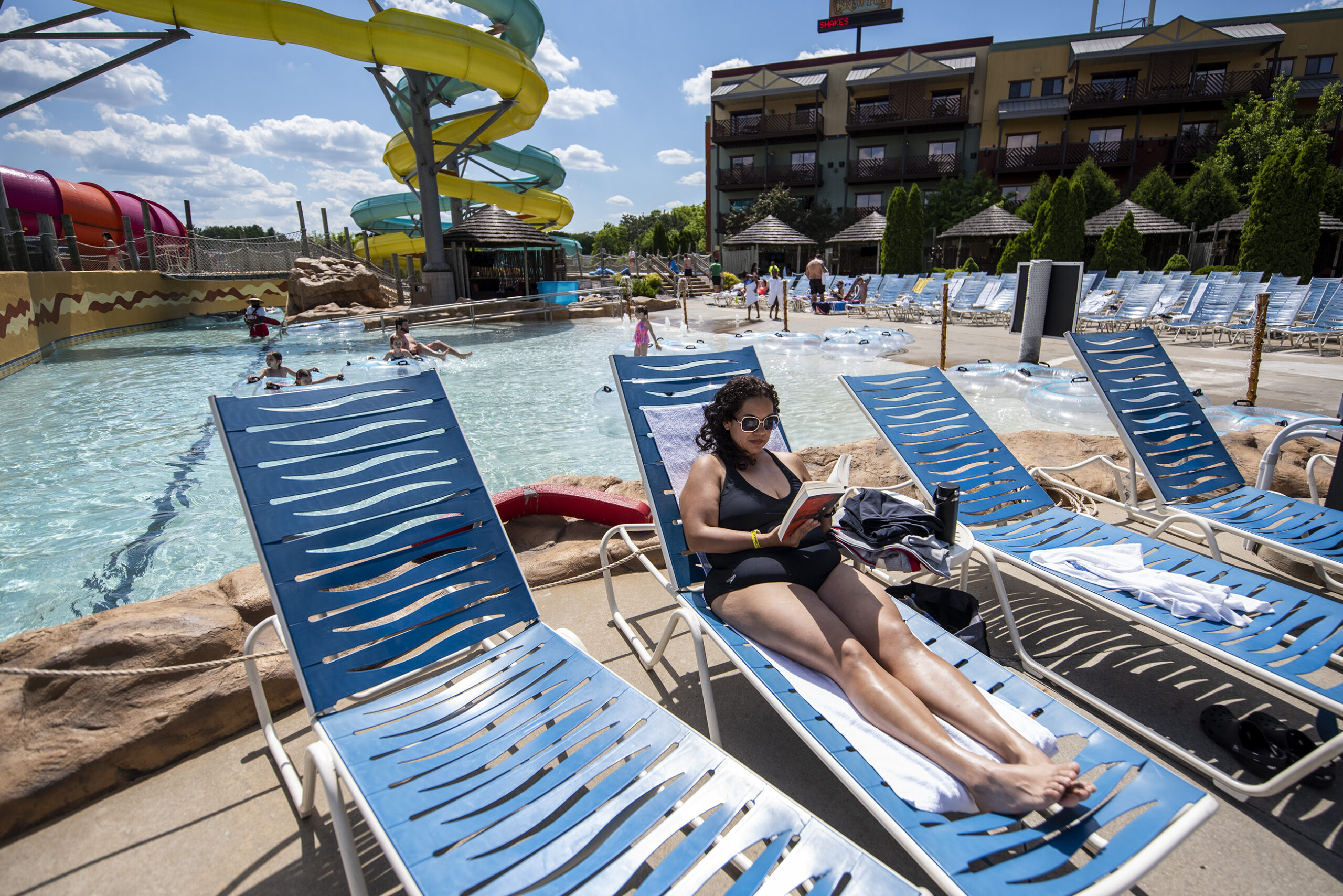 A woman sits in a chair near a pool as she reads a book in her swim suit.