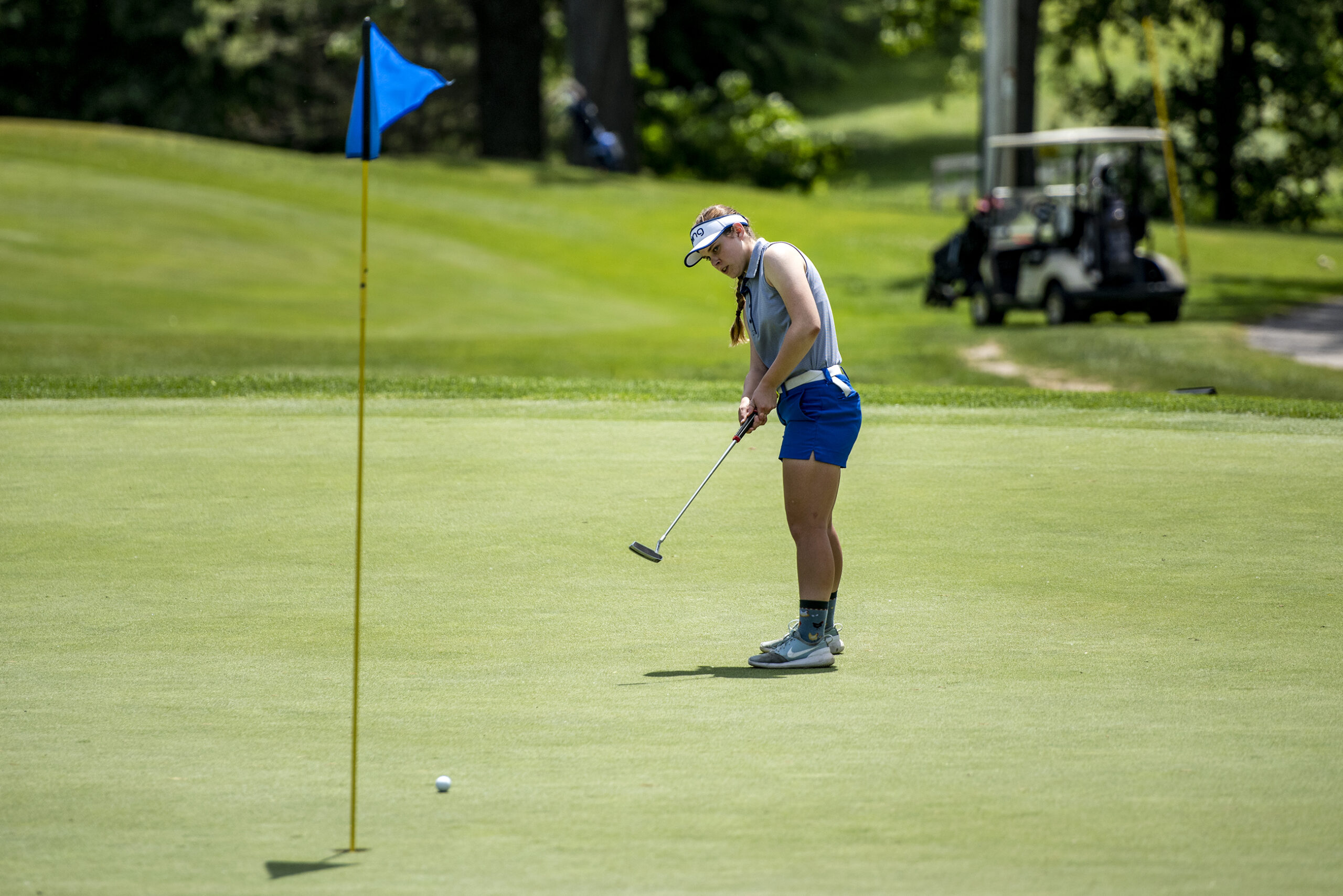 A girl watches as her ball rolls toward a hole marked with a blue flag.