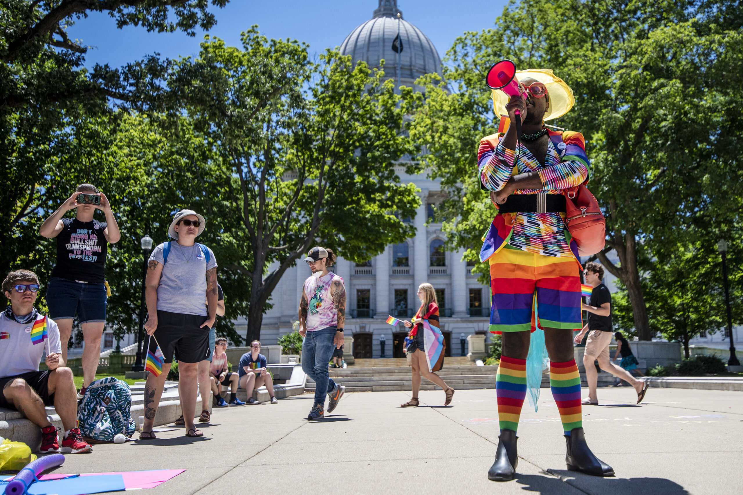 An activist in a rainbow striped outfit speaks into a megaphone outside the state capitol.