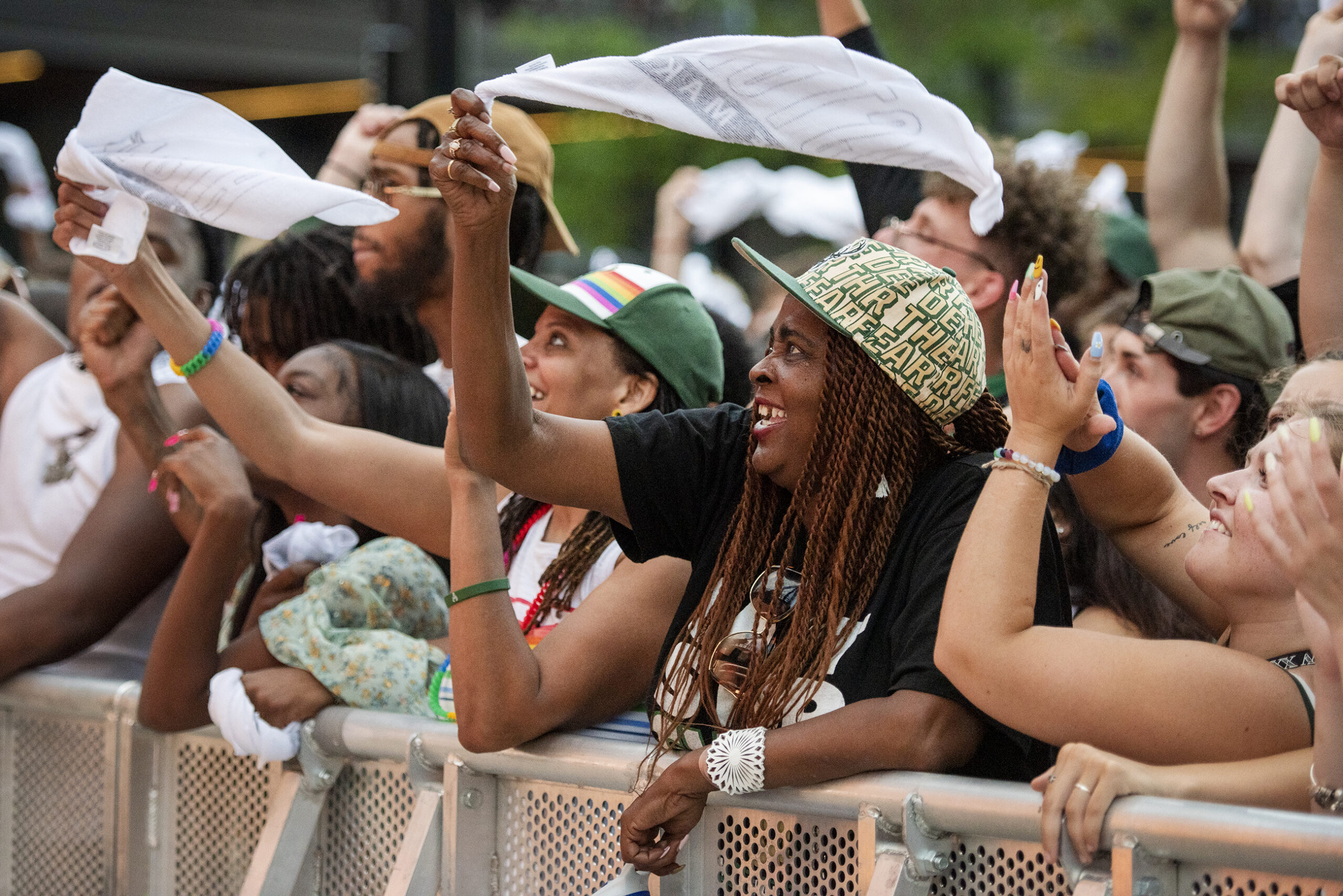 A fan wears a Bucks hat and waves a towel while watching the game in a crowd of people.