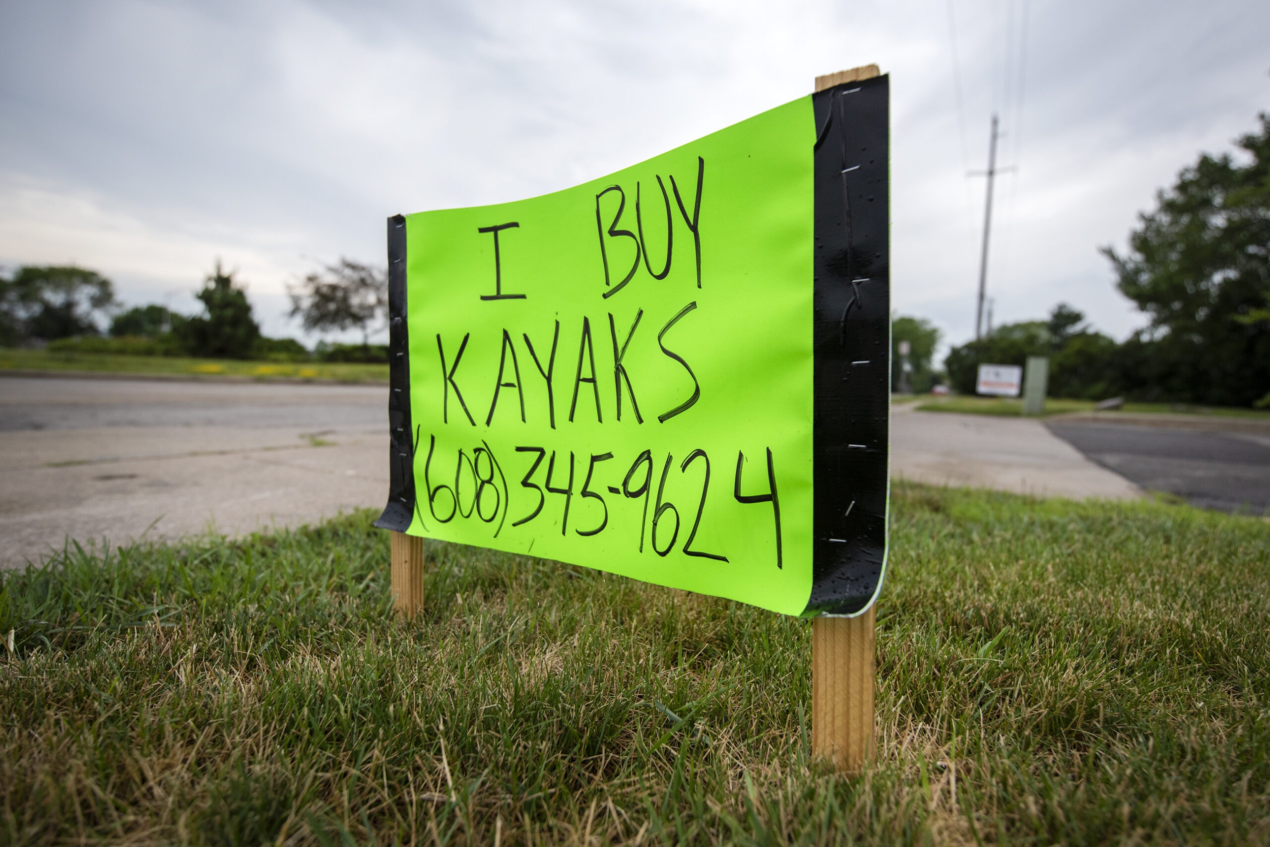 A green handmade sign says "I buy kayaks," followed by a phone number.
