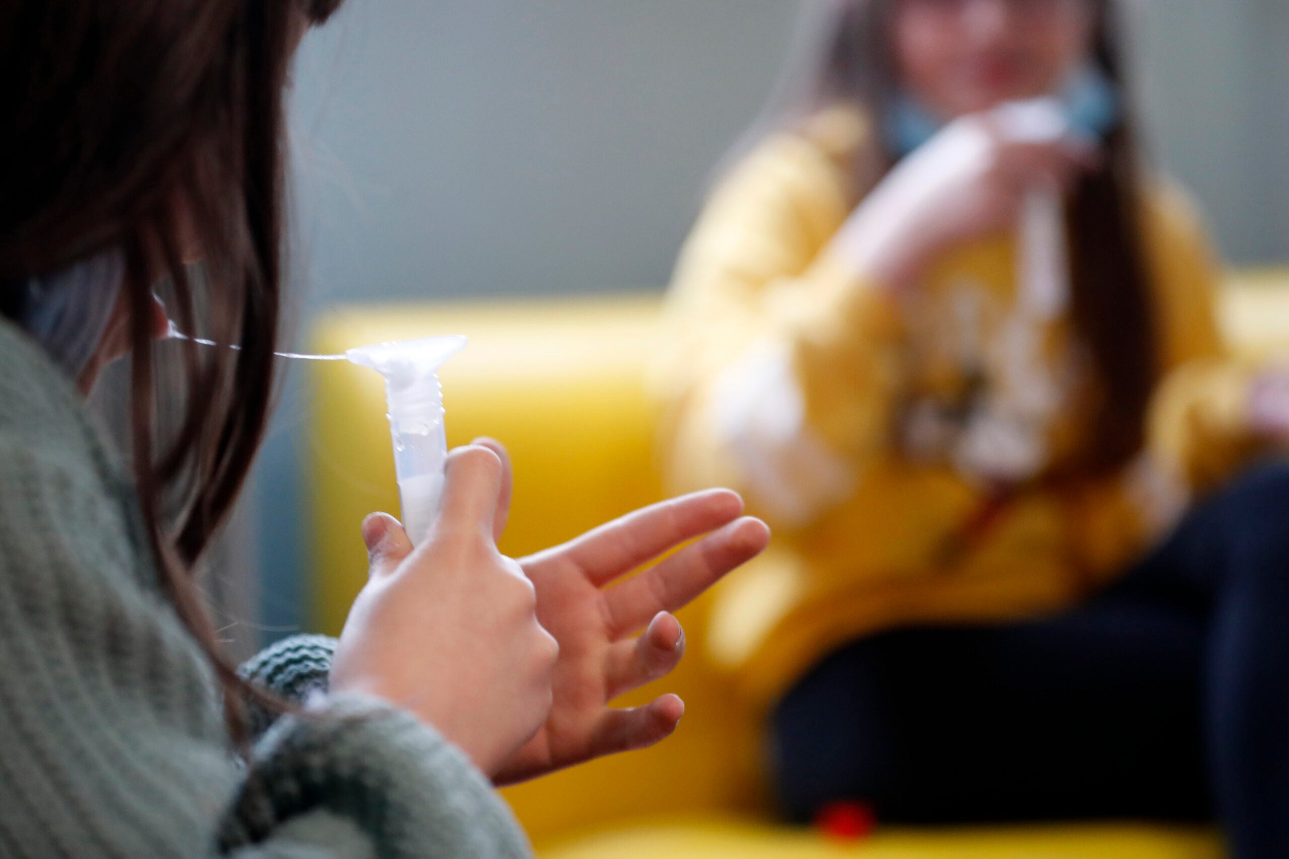 A child spits into a tube during a saliva COVID-19 testing session