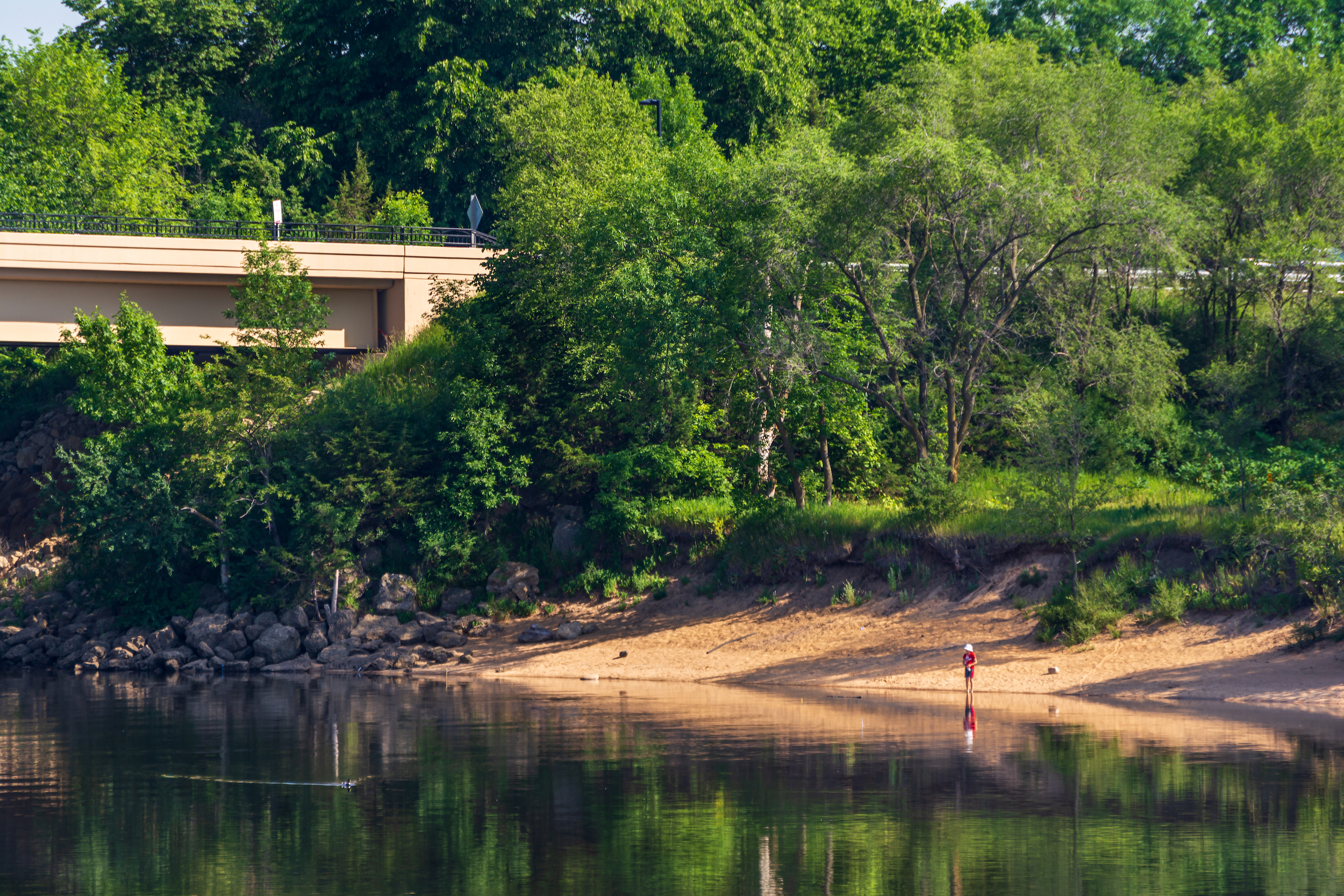A person fishes from shore along the Wisconsin River in Prairie du Sac, Wis.