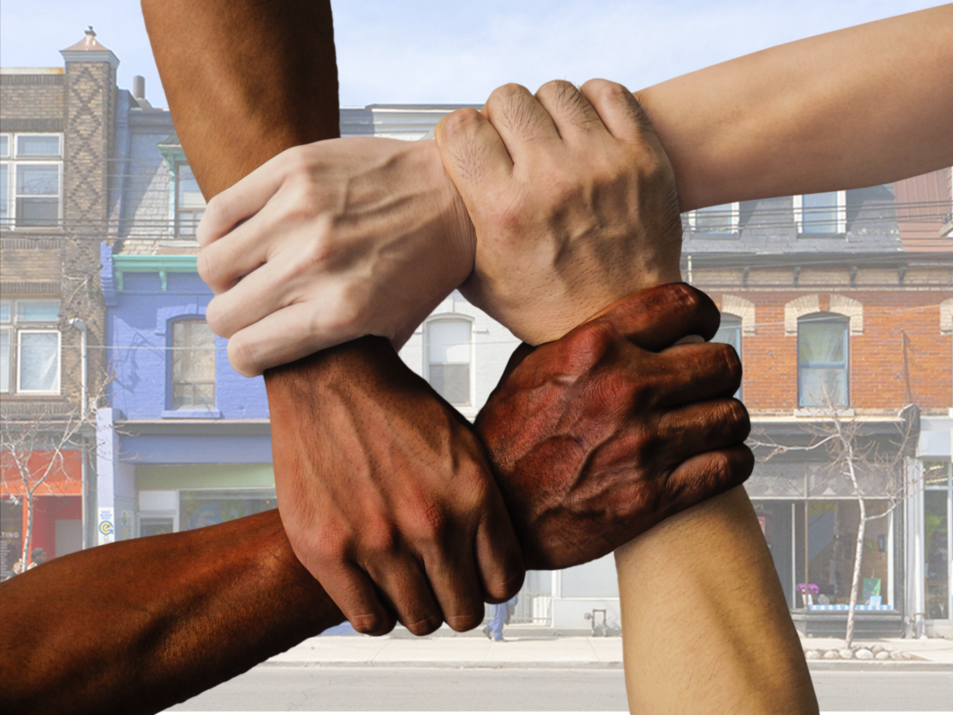 Hands of different skin tones clasping in front of a city streetscape.