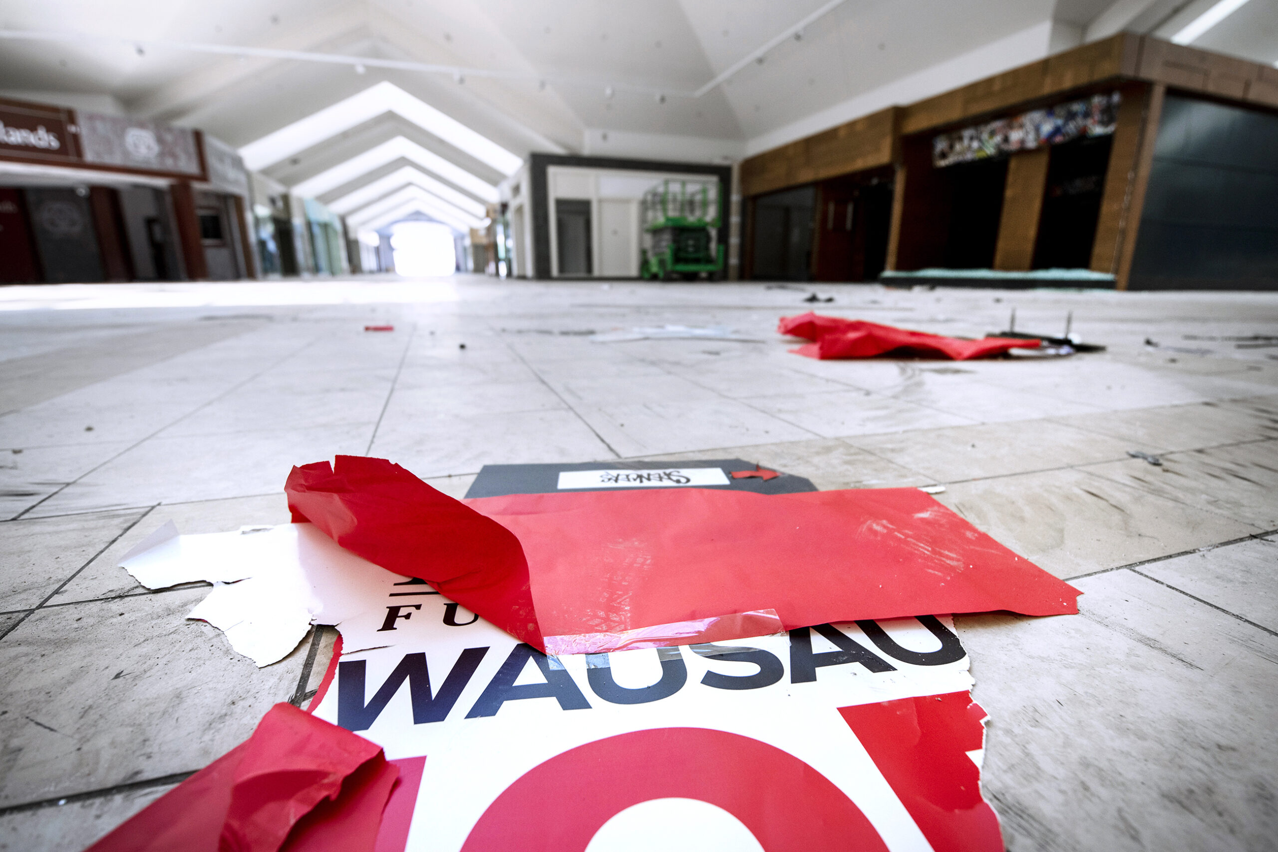 A ripped poster that says "WAUSAU" on it can be seen on a white tile floor inside of a mall.