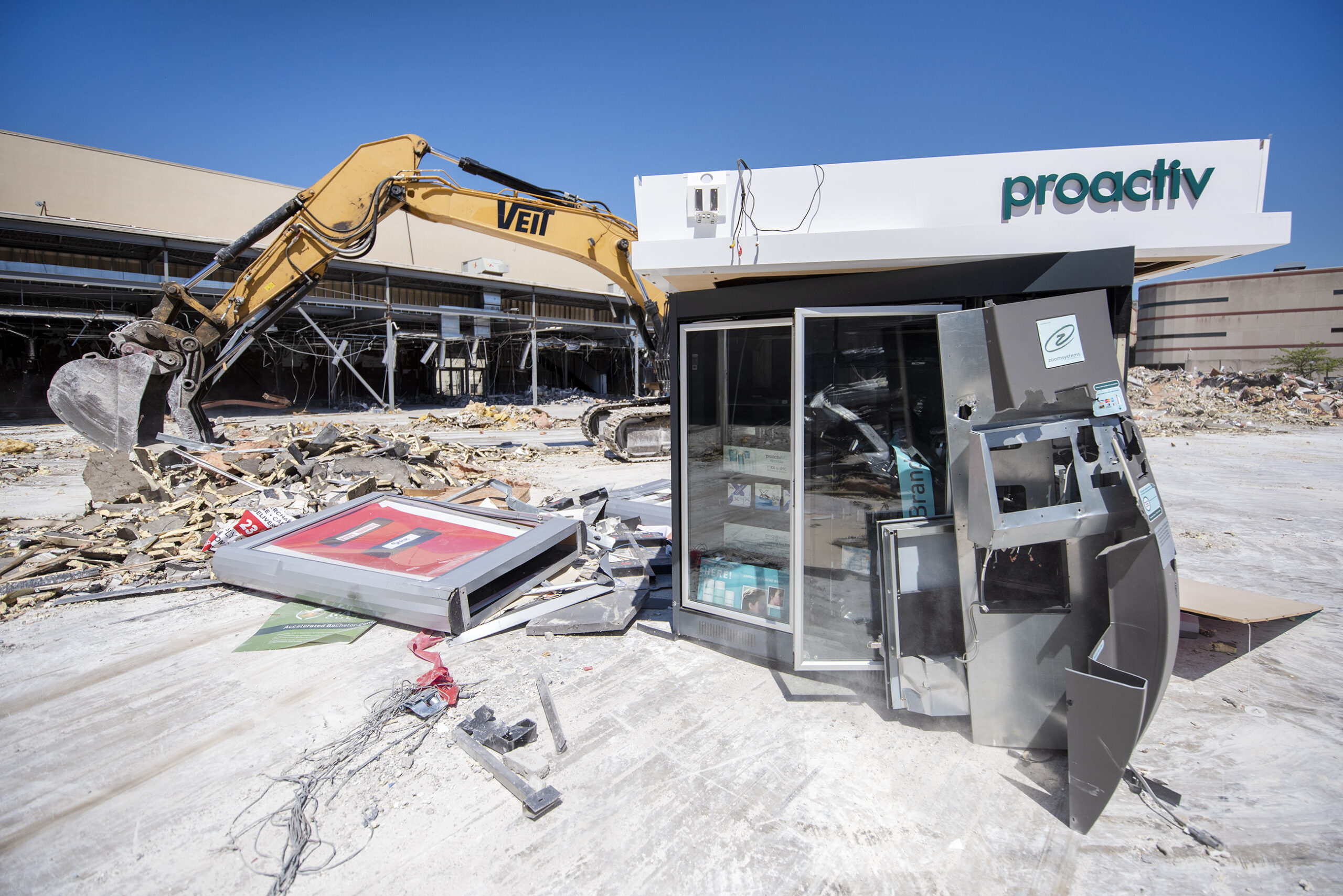 A Proactiv kiosk is partially destroyed as an excavator moves debris behind it.