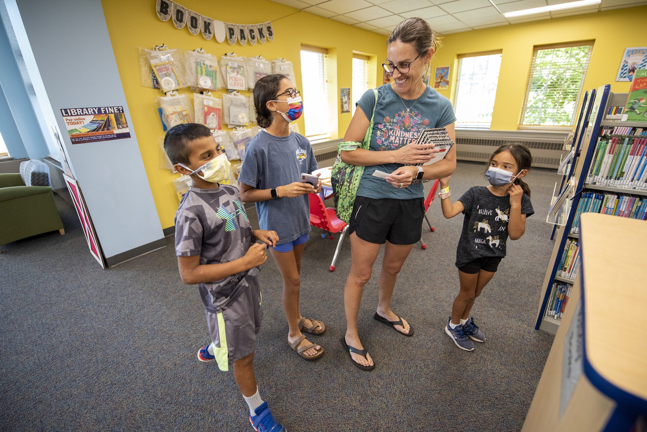 A woman smiles at her children who are wearing face masks in the library.