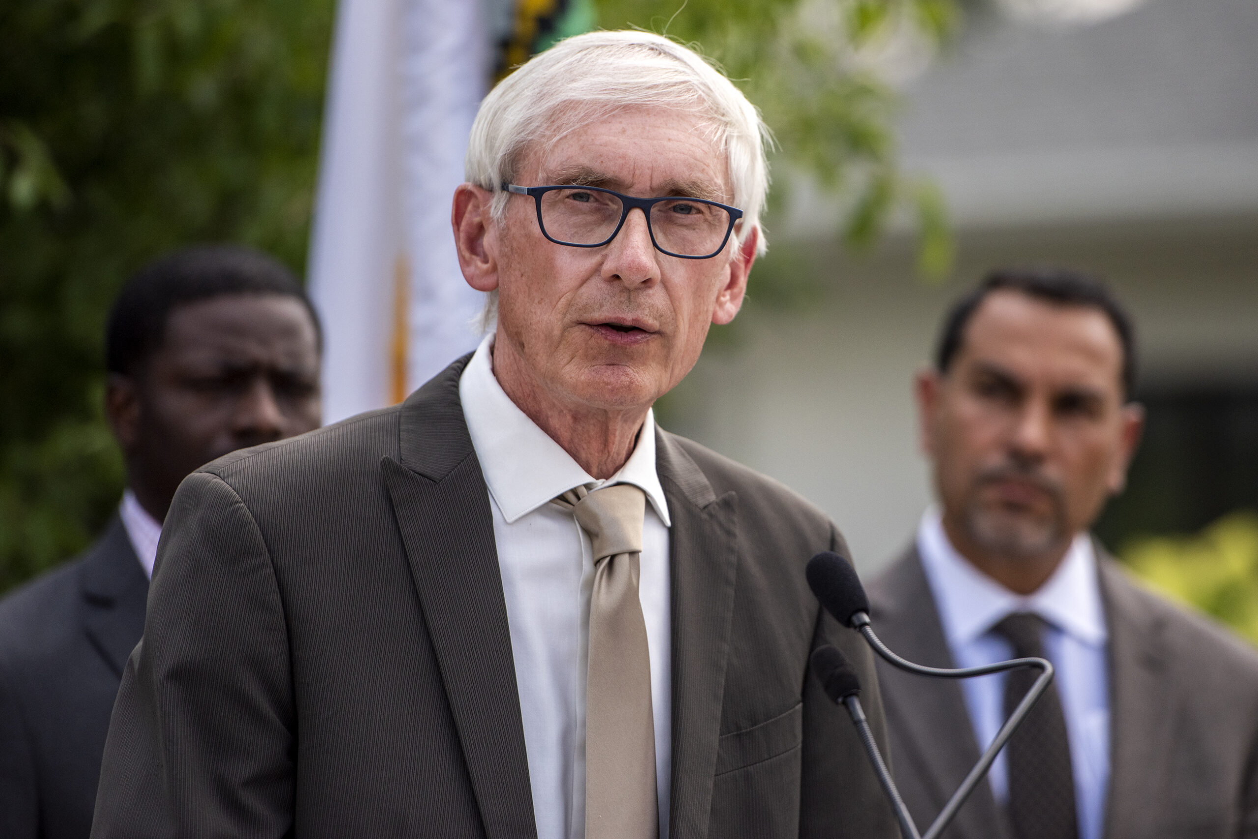 Gov. Tony Evers stands outside at a microphone during a press conference.