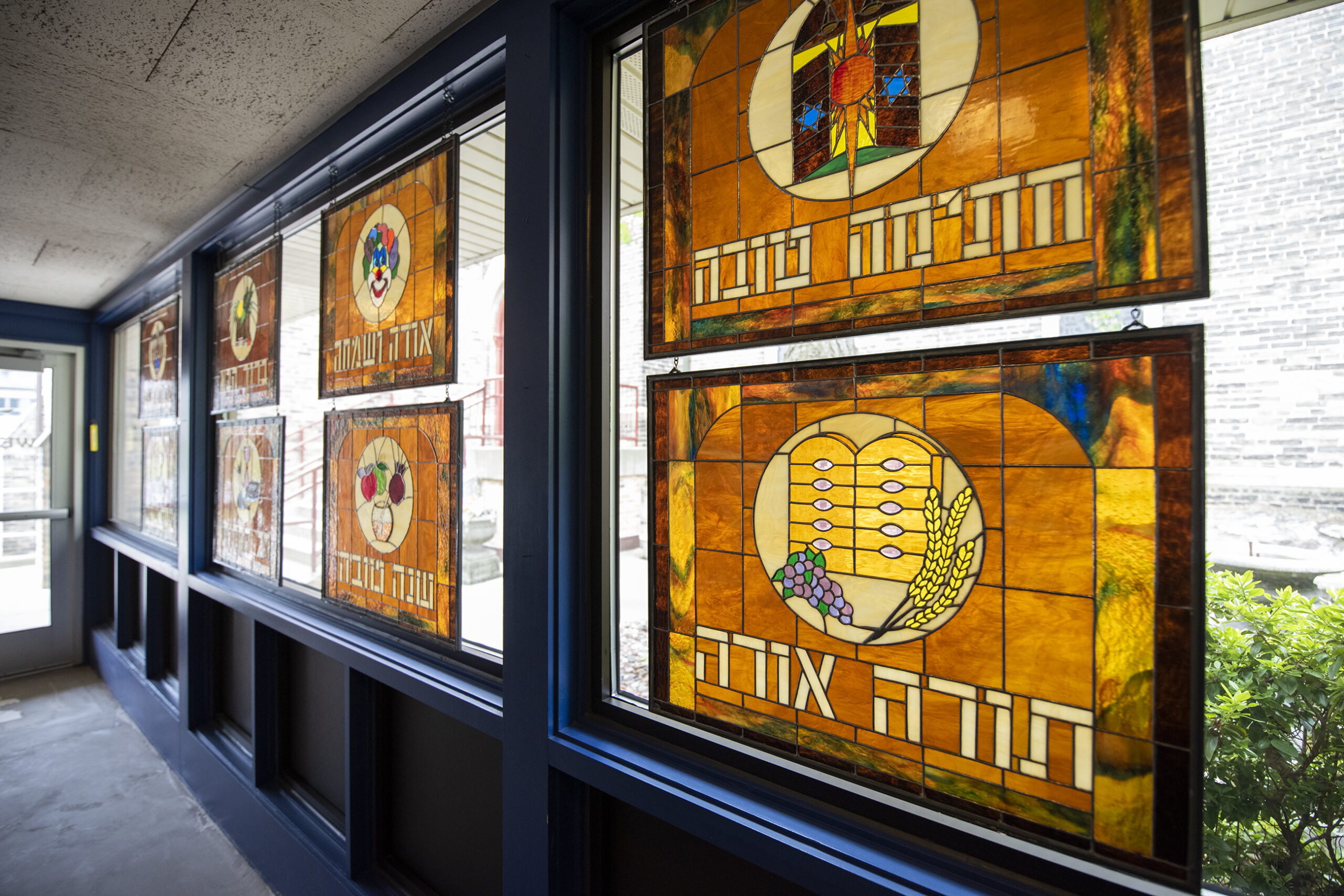 Amber colored stained glass depicting different Jewish holidays are displayed on a window.