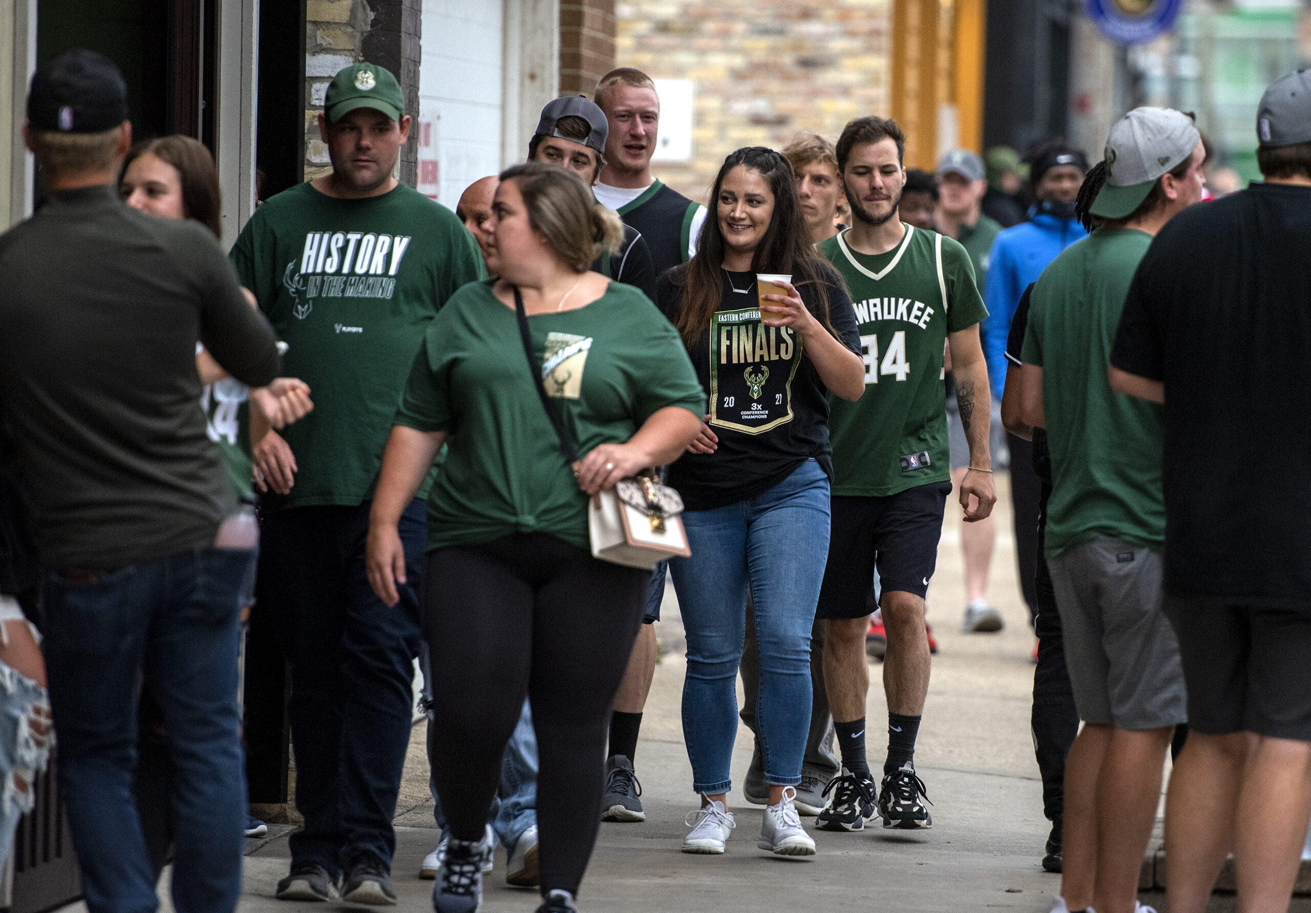 Fans in green Bucks jerseys drink beer as they walk outside.