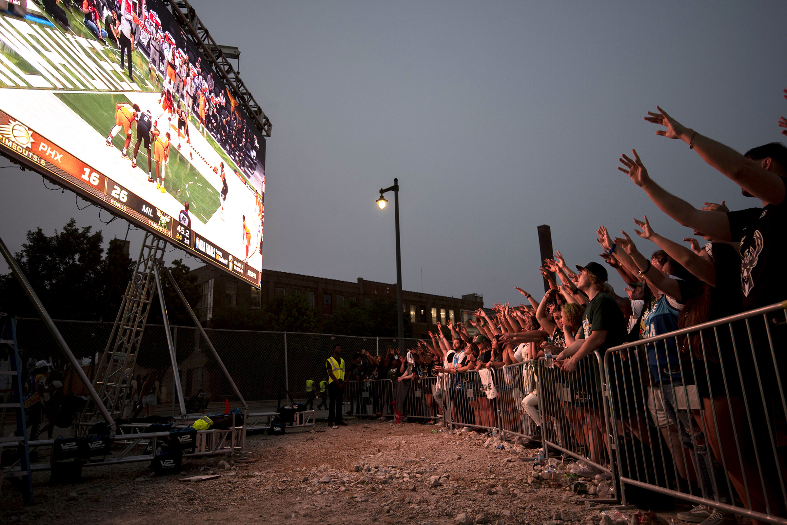 Fans raise their arms to a screen showing the game.
