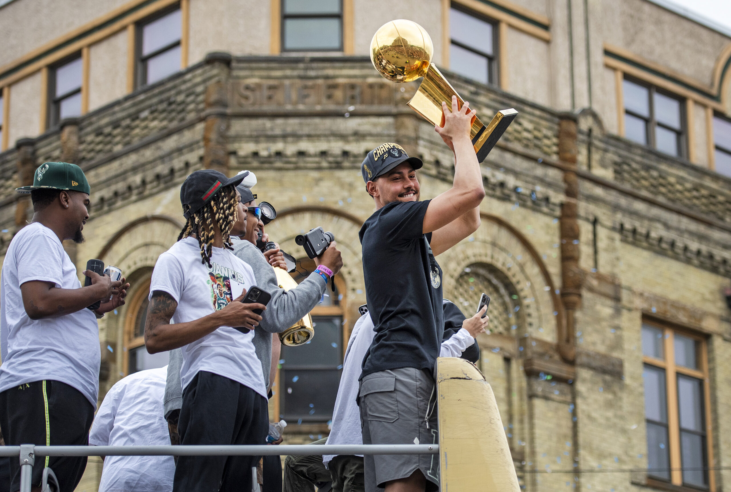 A Bucks player holds the trophy above his head from on top of a bus.