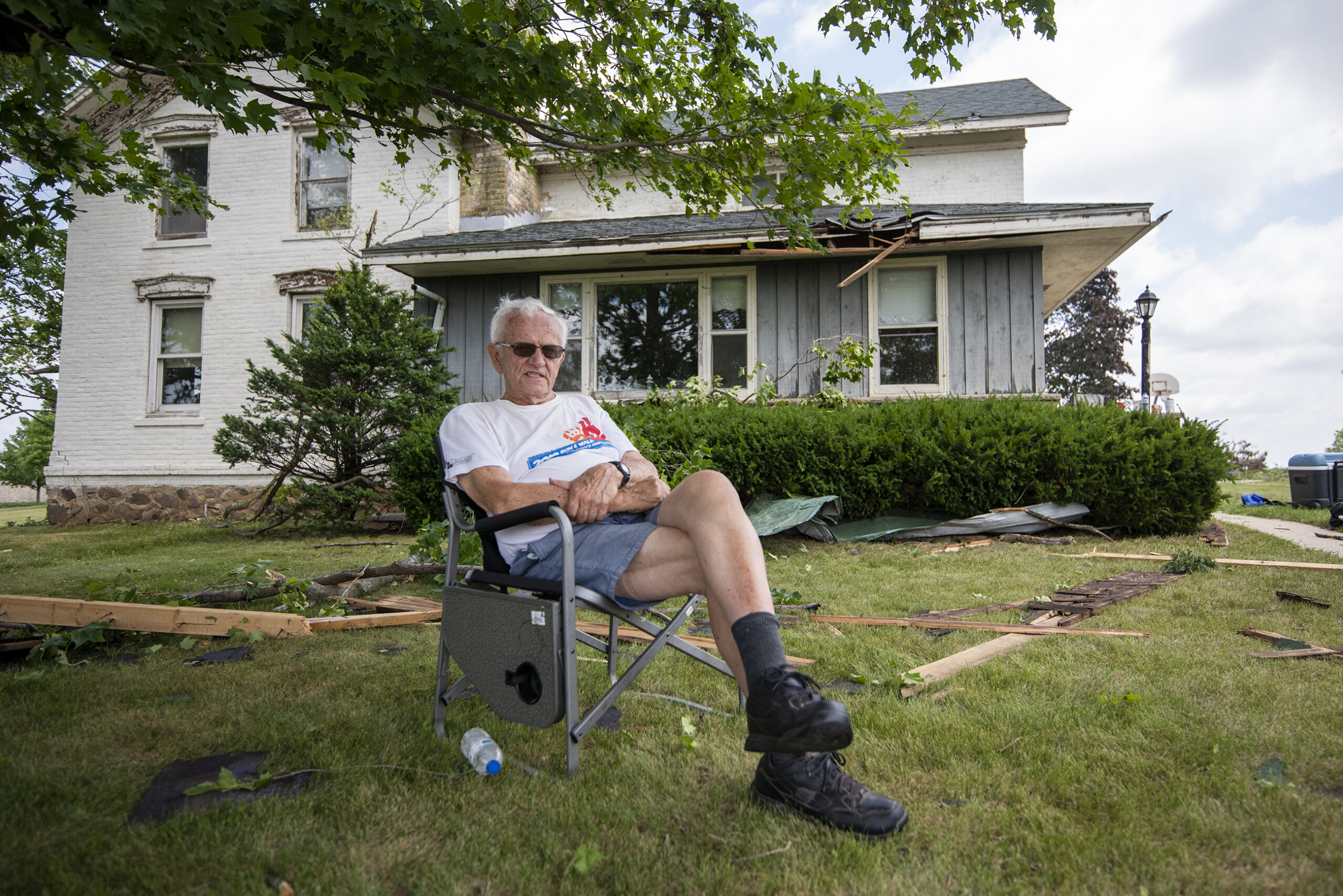 A man in sunglasses sits in a lawn chair in front of his home.