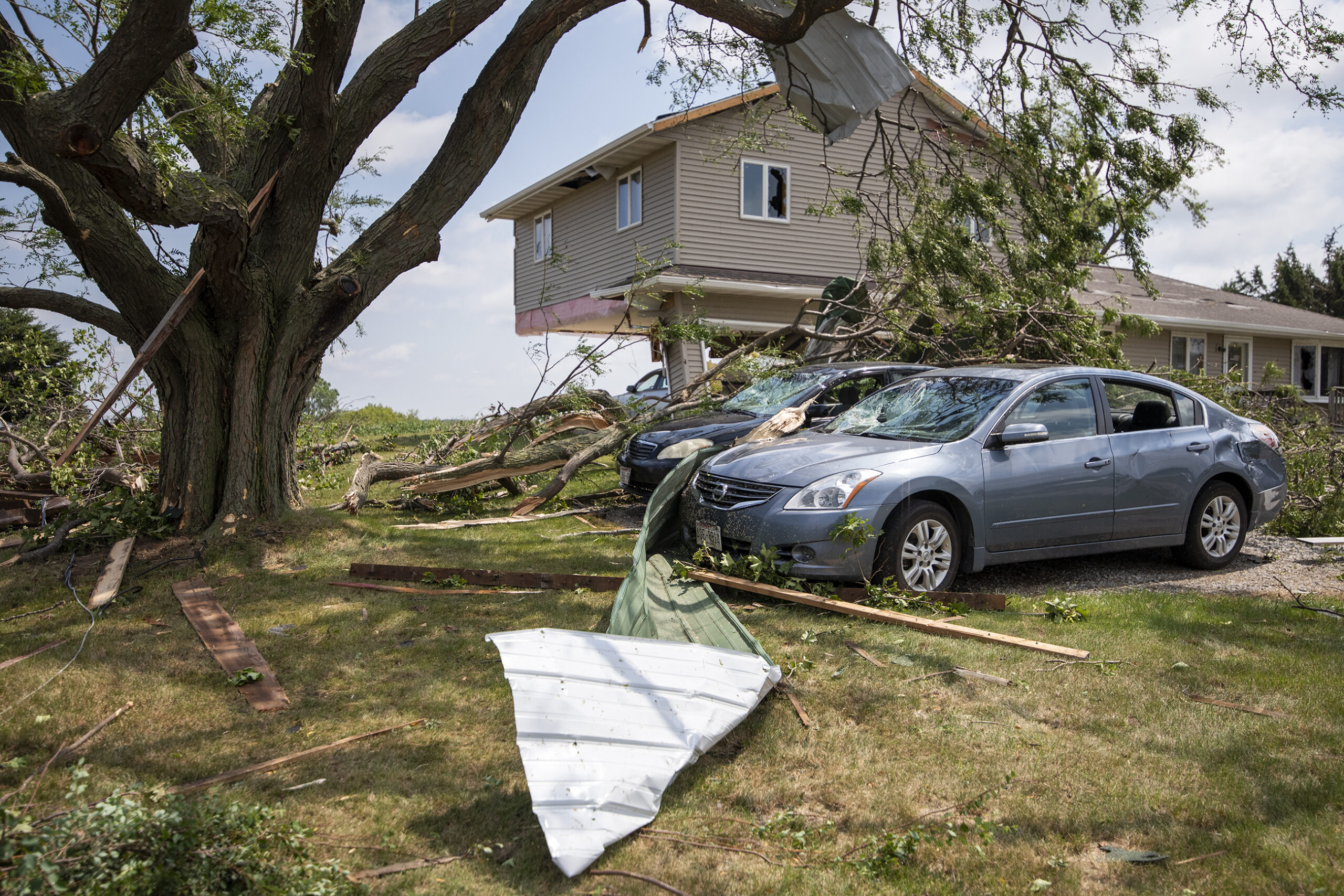 Two damaged vehicles sit next to a home with severe storm damage.
