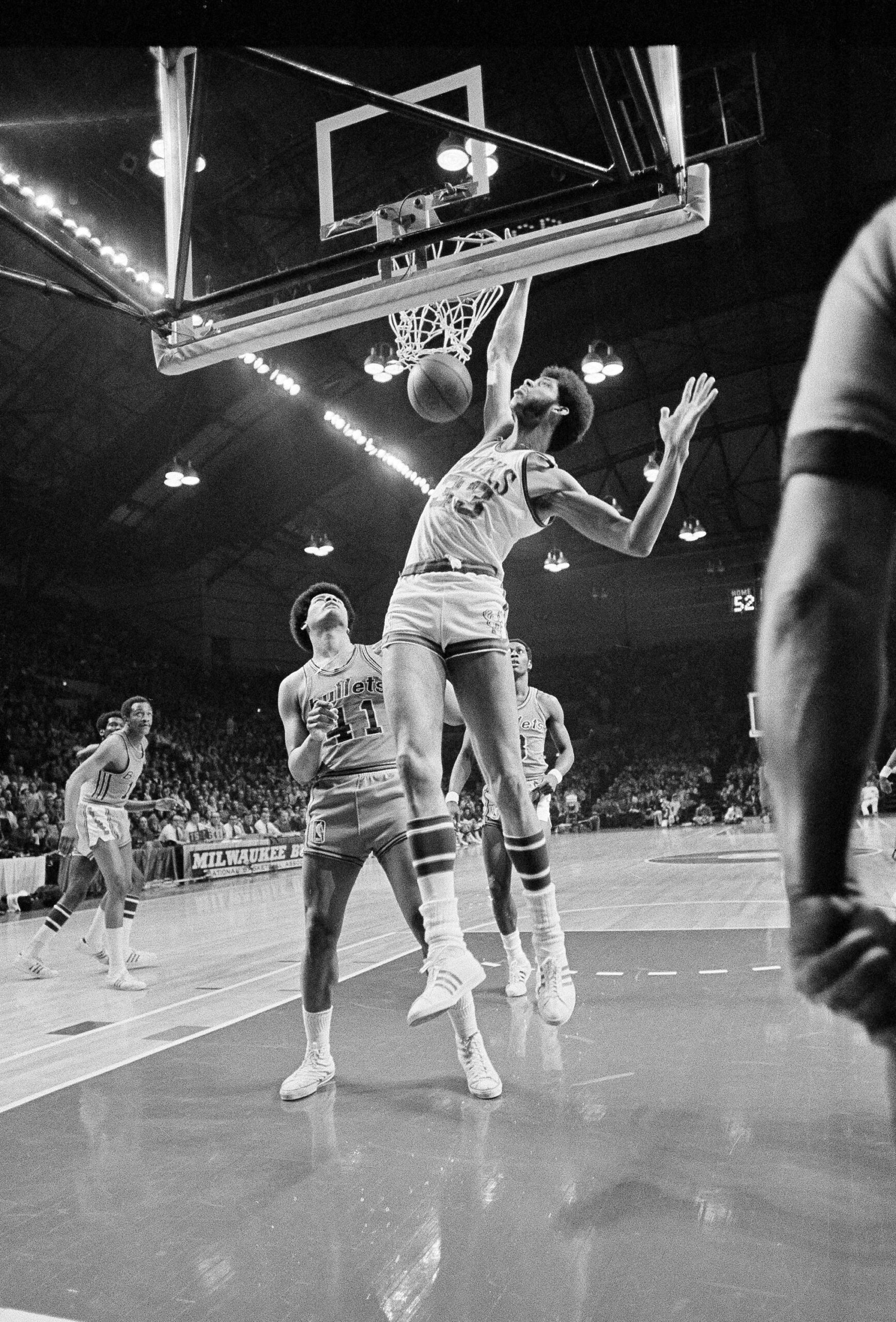 Baltimore Bullets' Wes Unseld watches as Bucks Lew Alcindor, now, Kareem Abdul-Jabbar, dunks a basketball