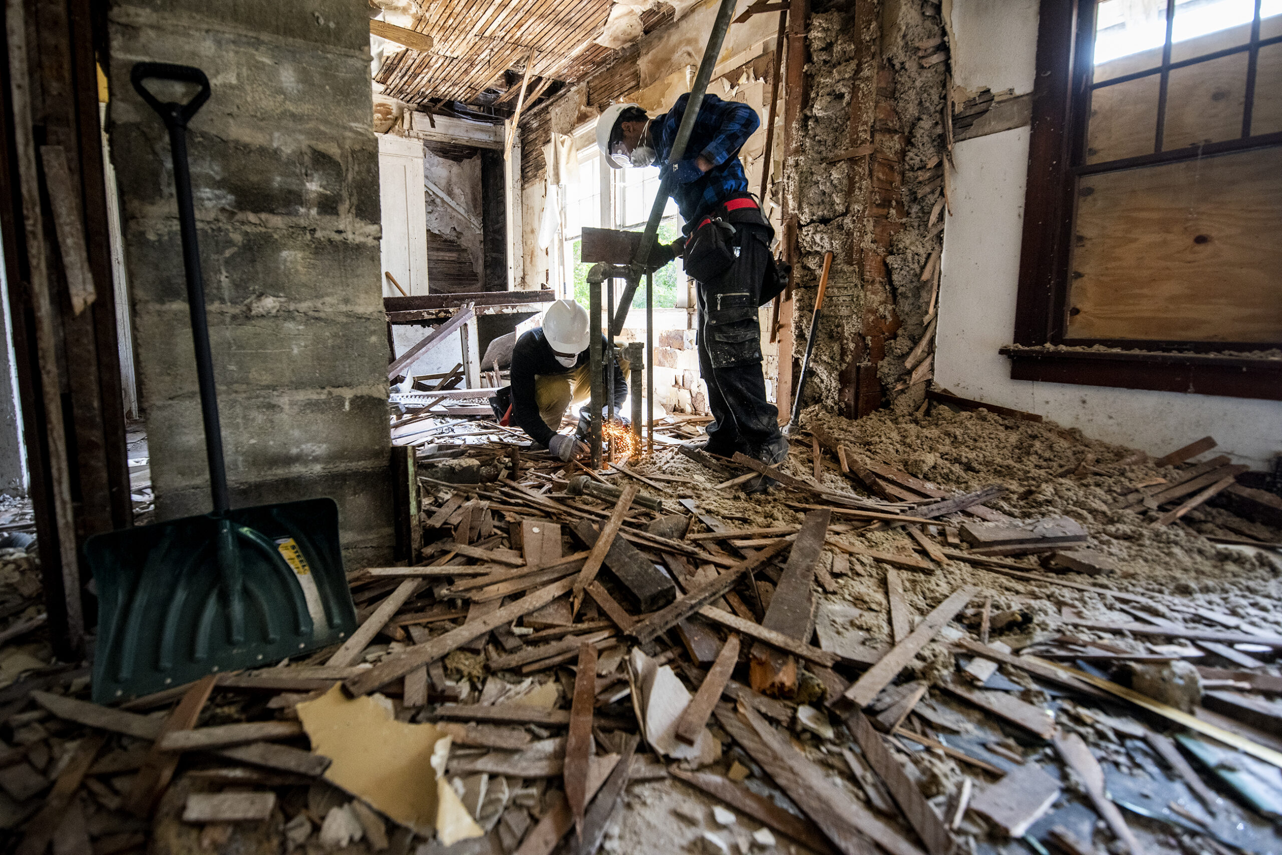 Wood and debris cover the floor as a worker further deconstructs the room.