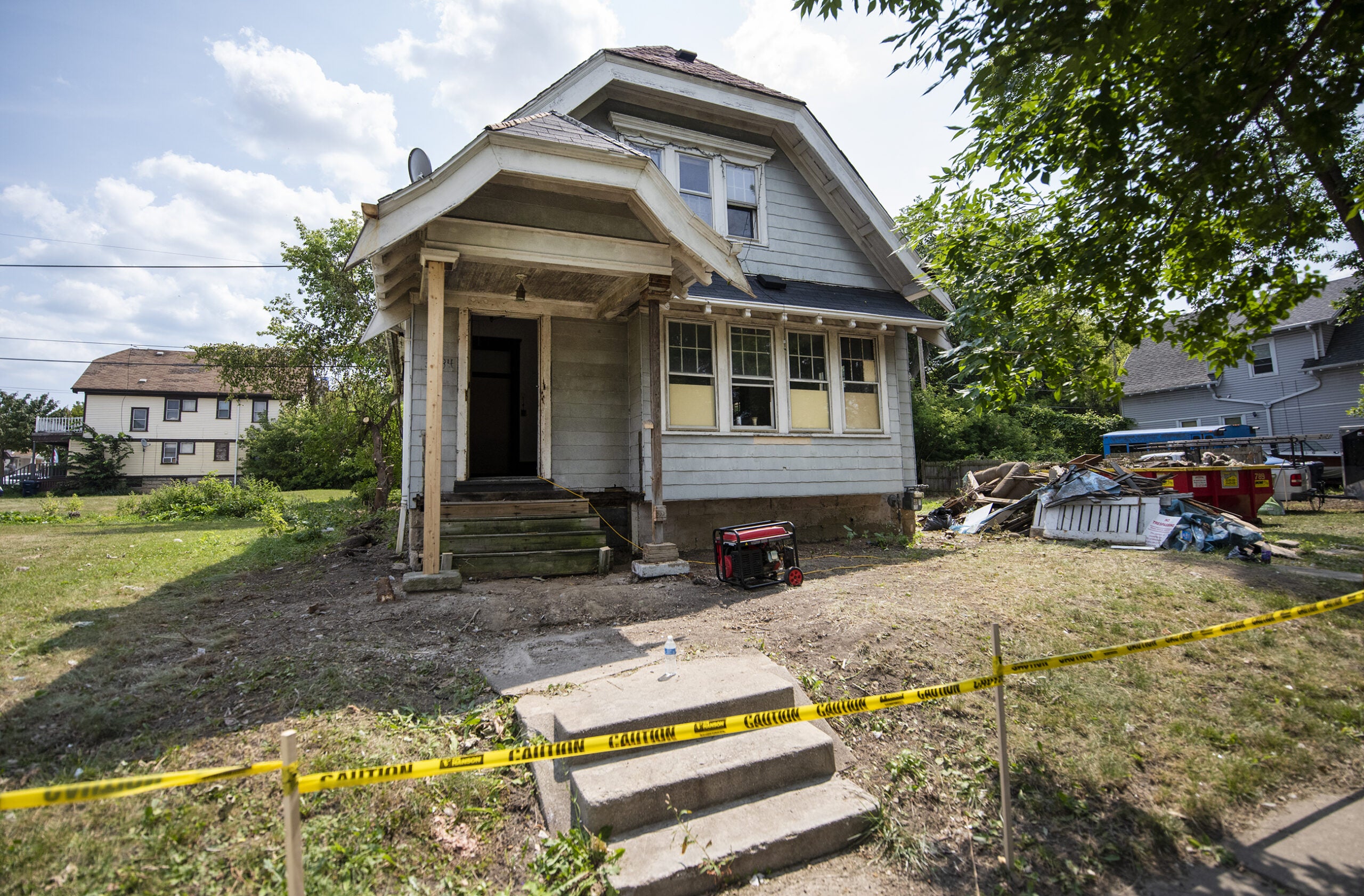 A blue home is mid-renovation. Yellow caution tape blocks off the front yard.