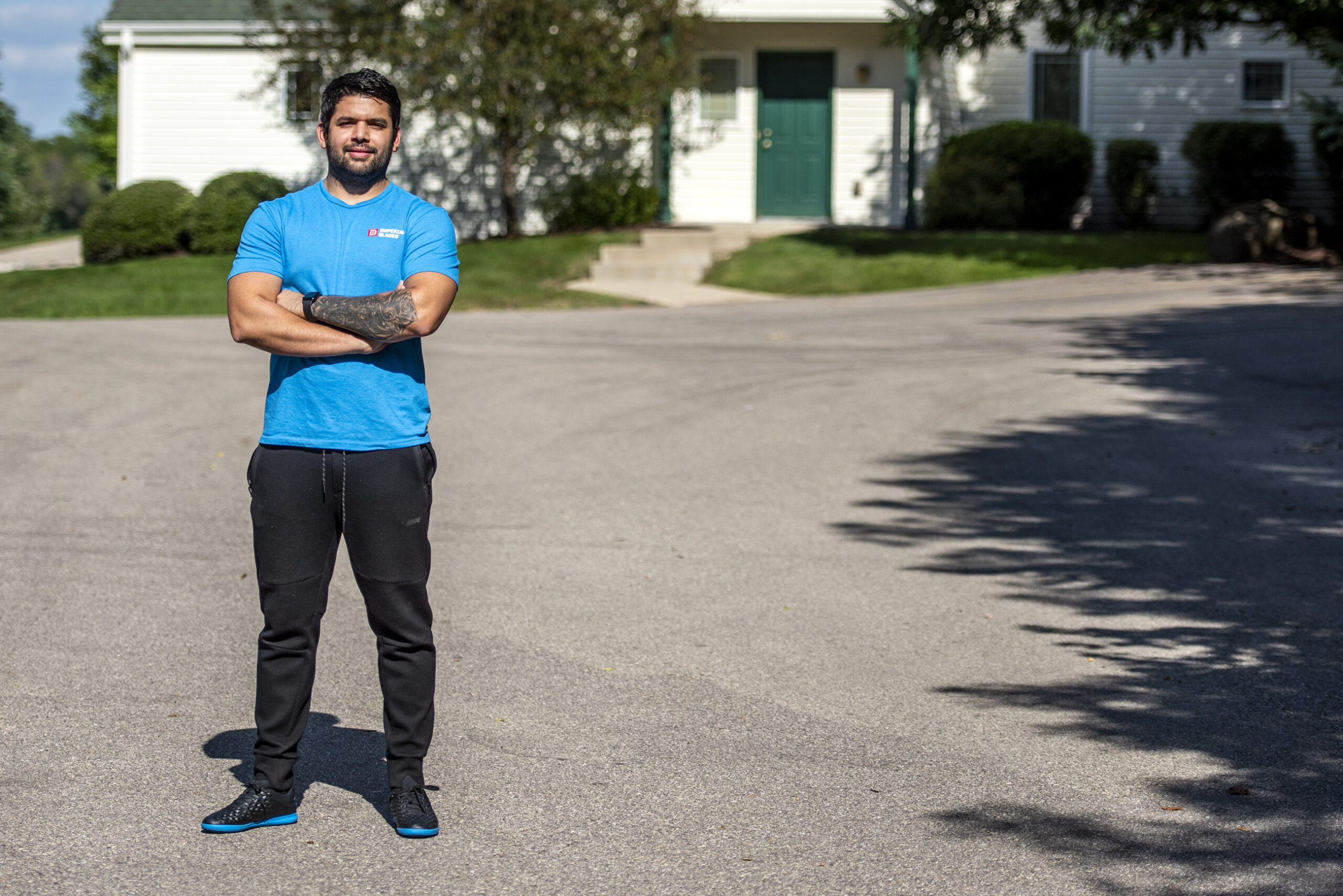 A man in a blue t-shirt stands outside in a neighborhood.