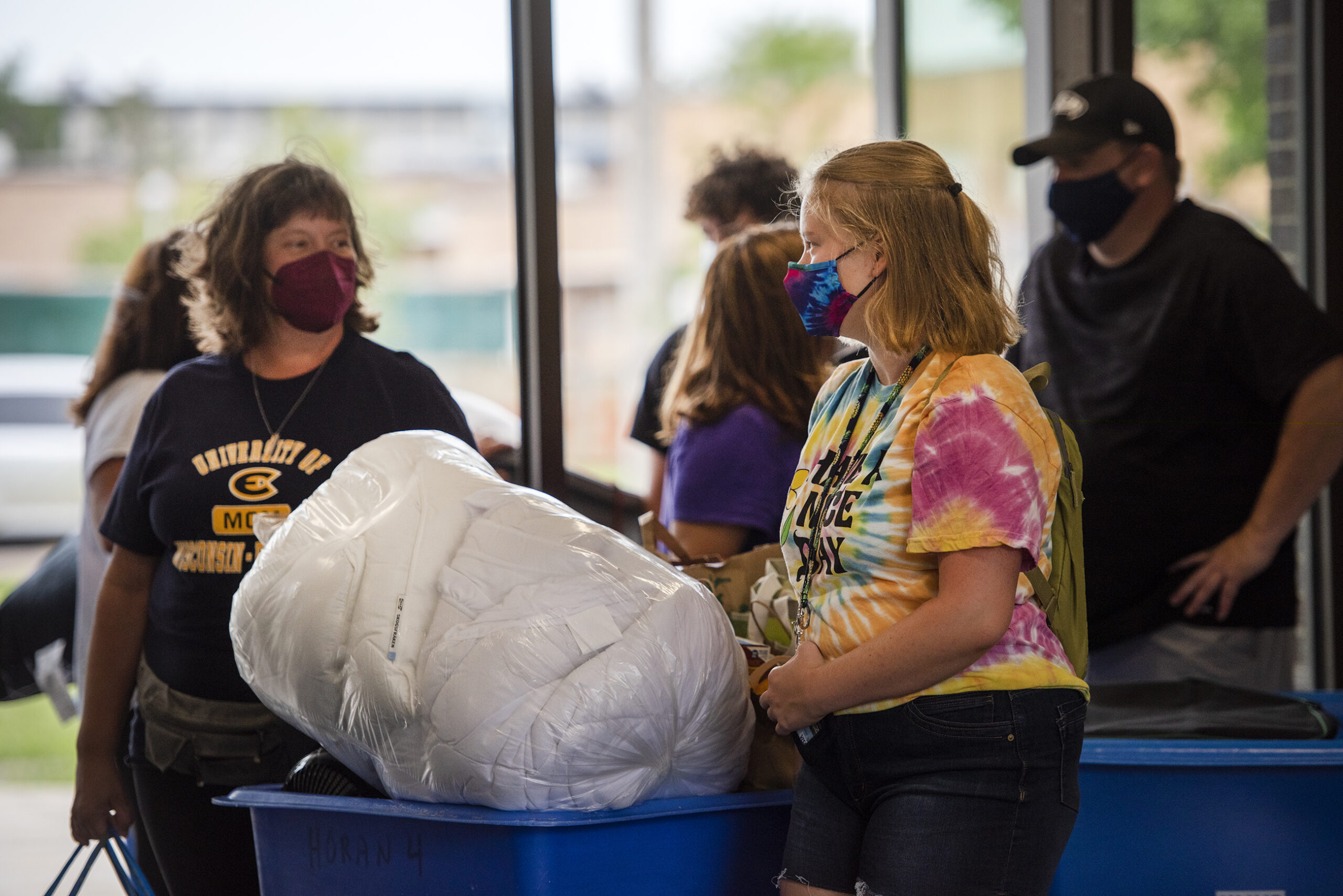People stand in a lobby near bins full of bedding and other items.