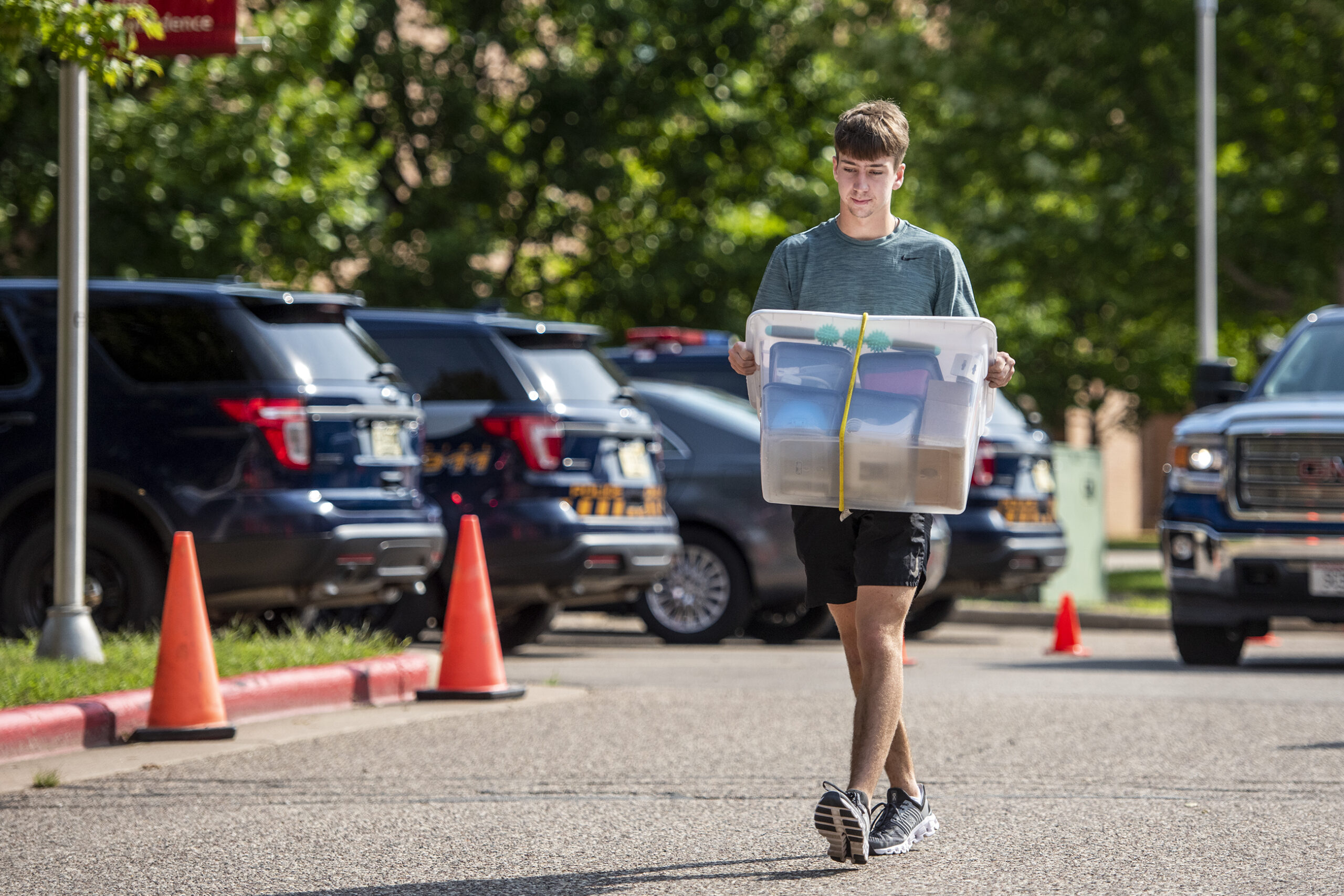 A student holds a clear plastic box as he walks through a parking lot.