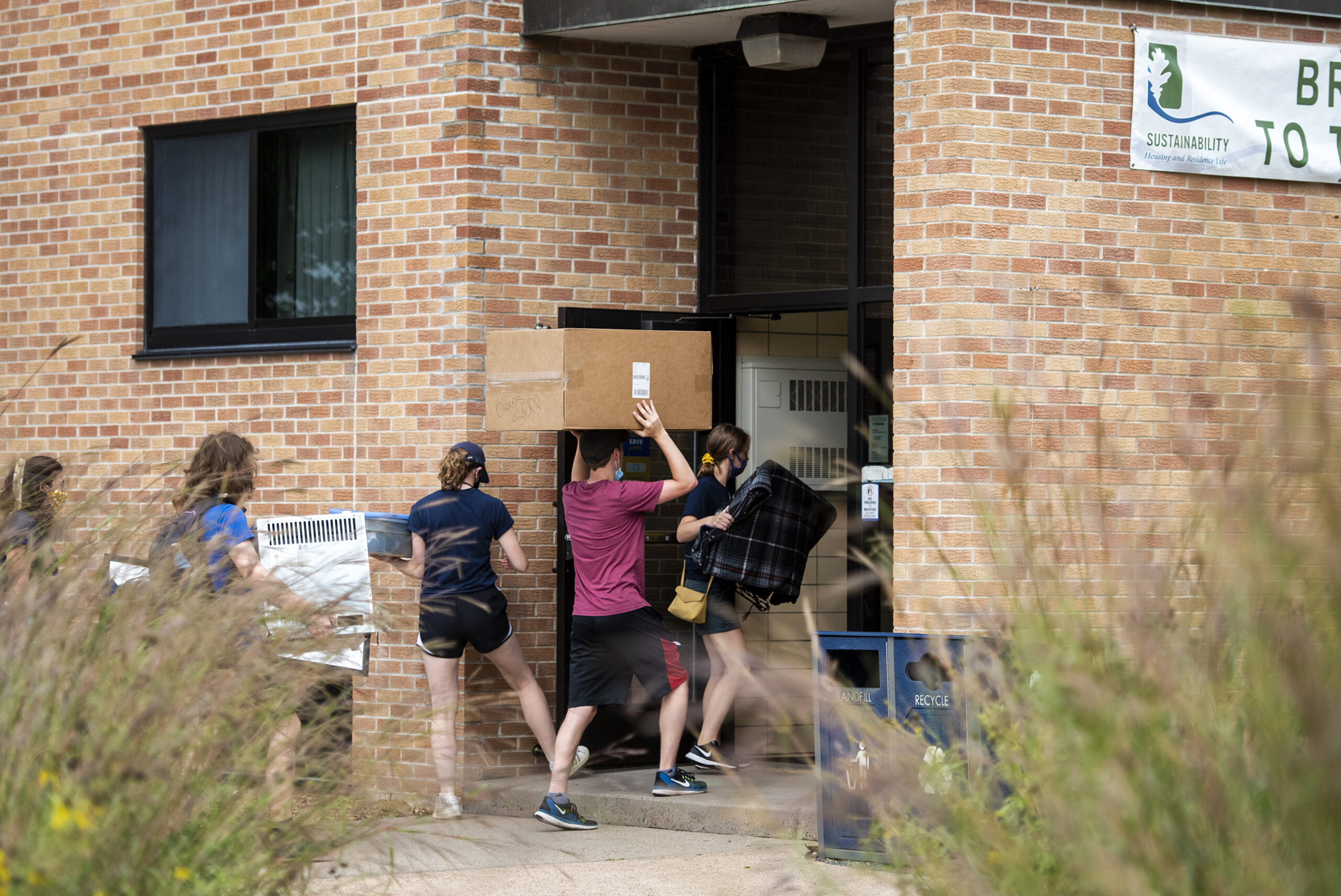 People walk through the door of a residence hall carrying boxes.