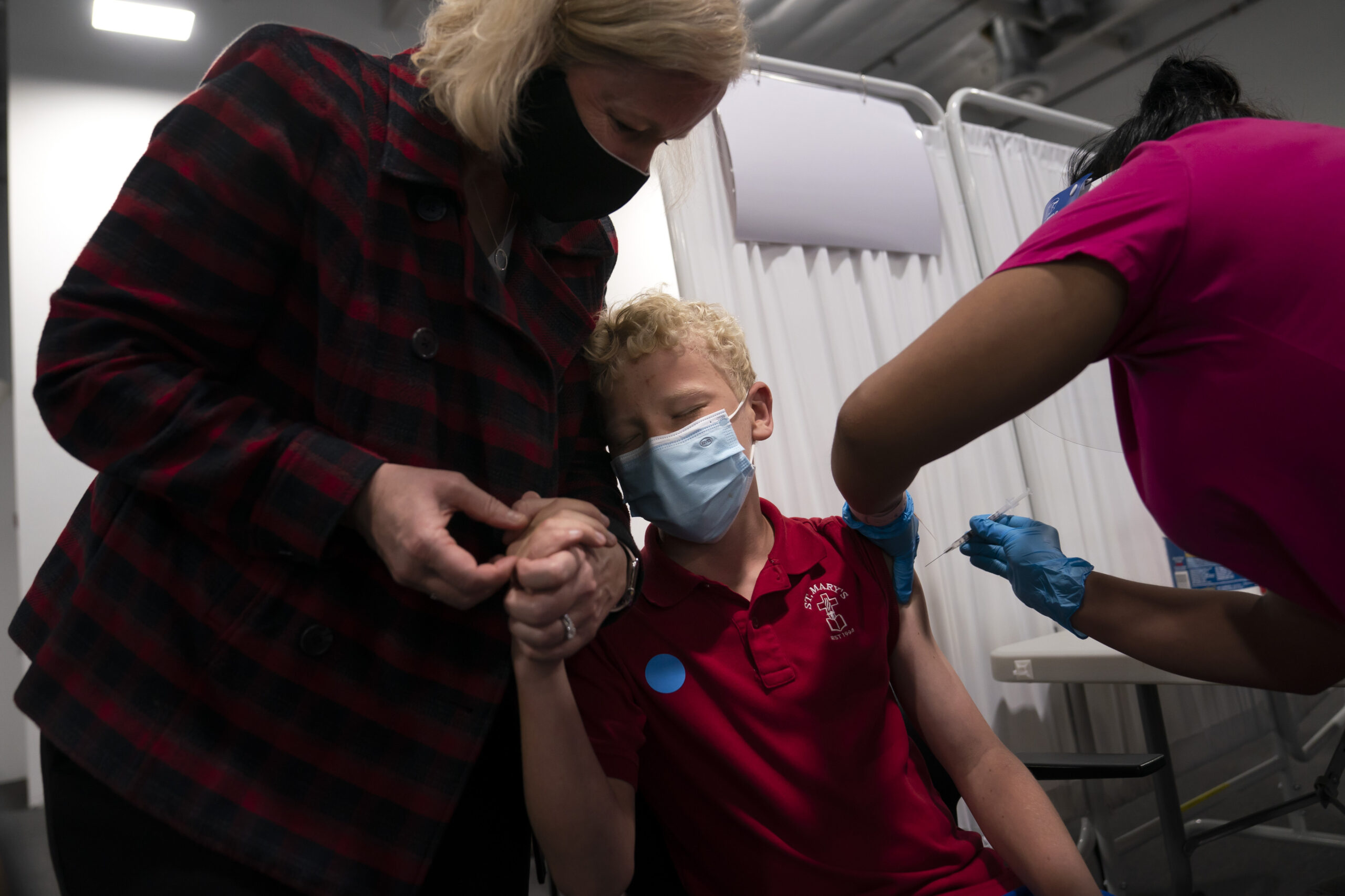 Heather Haworth holds the hand of her 12-year-old son Jeremy as he receives the first dose of the Pfizer COVID-19 vaccine.