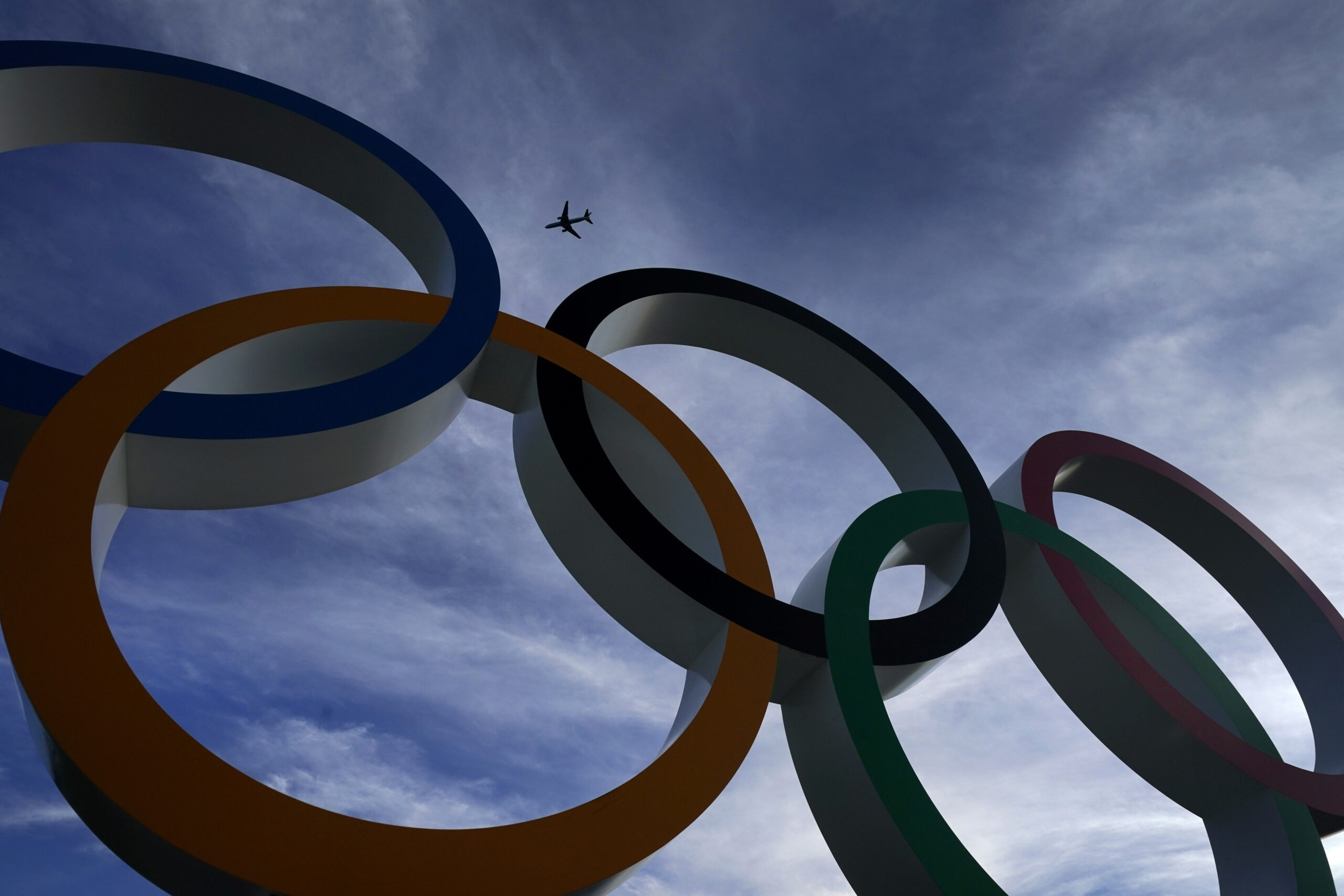 A passenger jet flies over the Olympic rings on display outside the Olympic Stadium