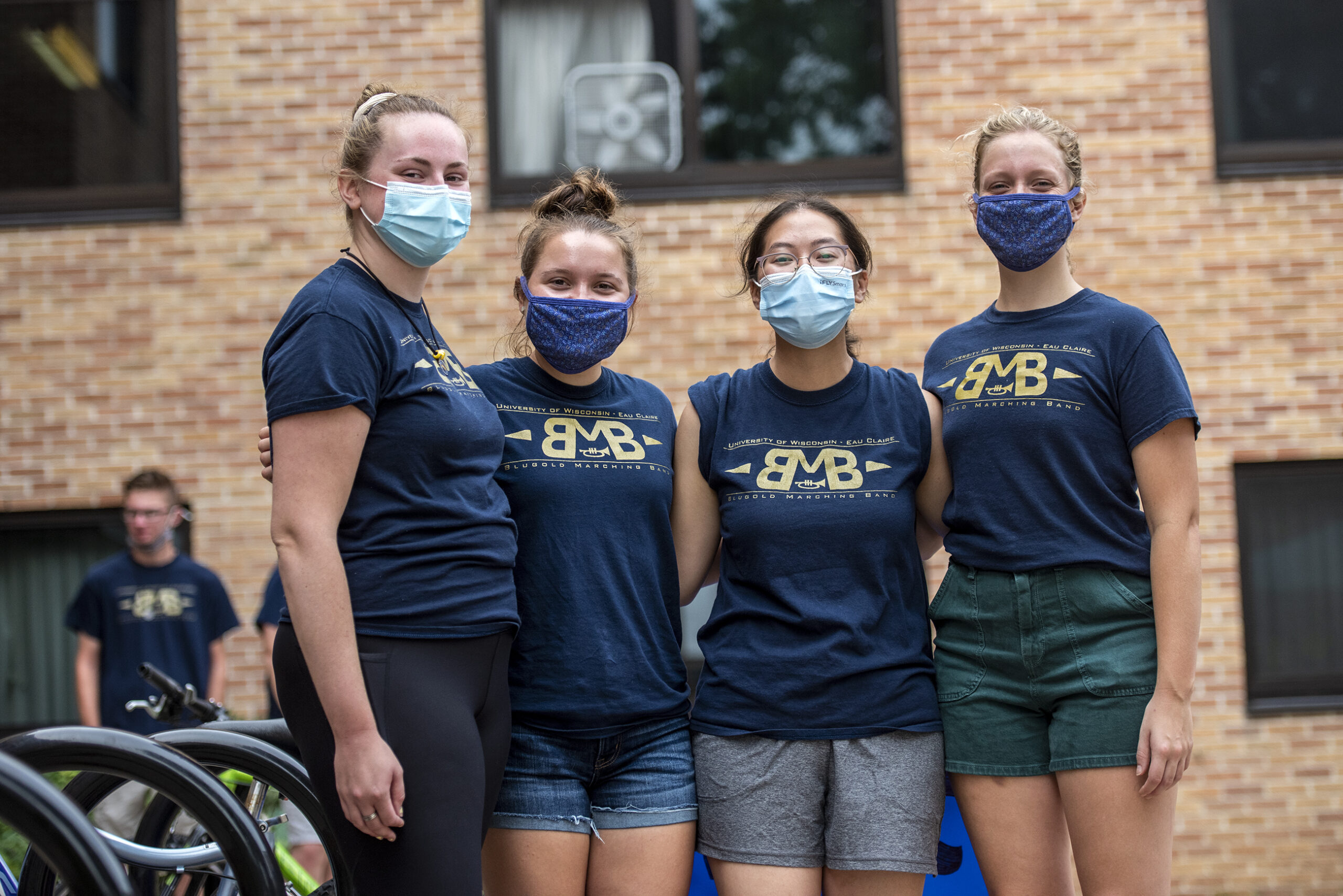 Four girls wear face masks as they stand together.