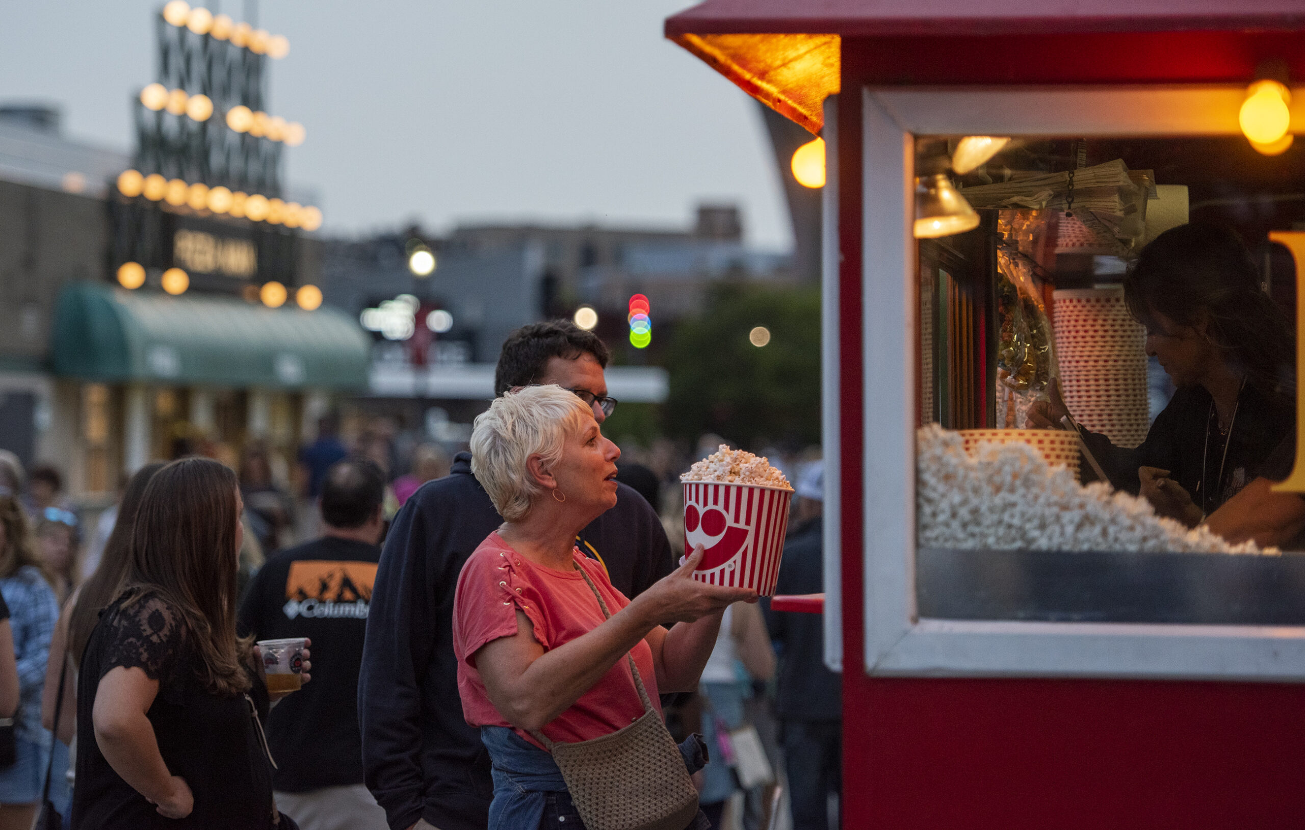 A woman receives a bucket of popcorn from a booth.