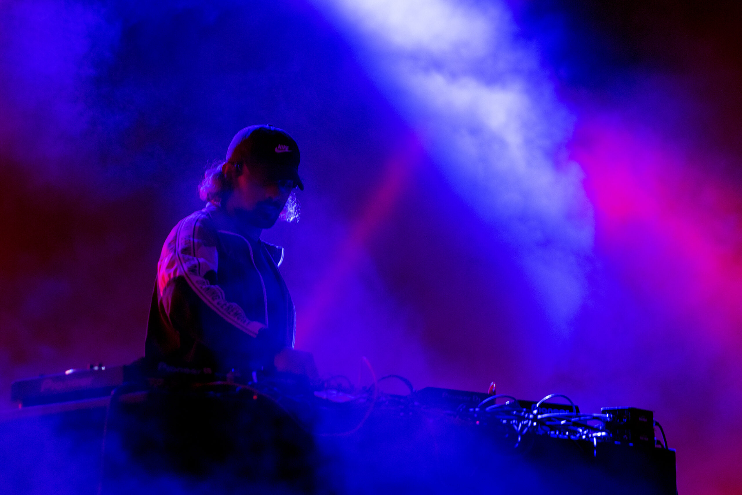 Blue and purple light catches the smoke surrounding a DJ as he plays a set.