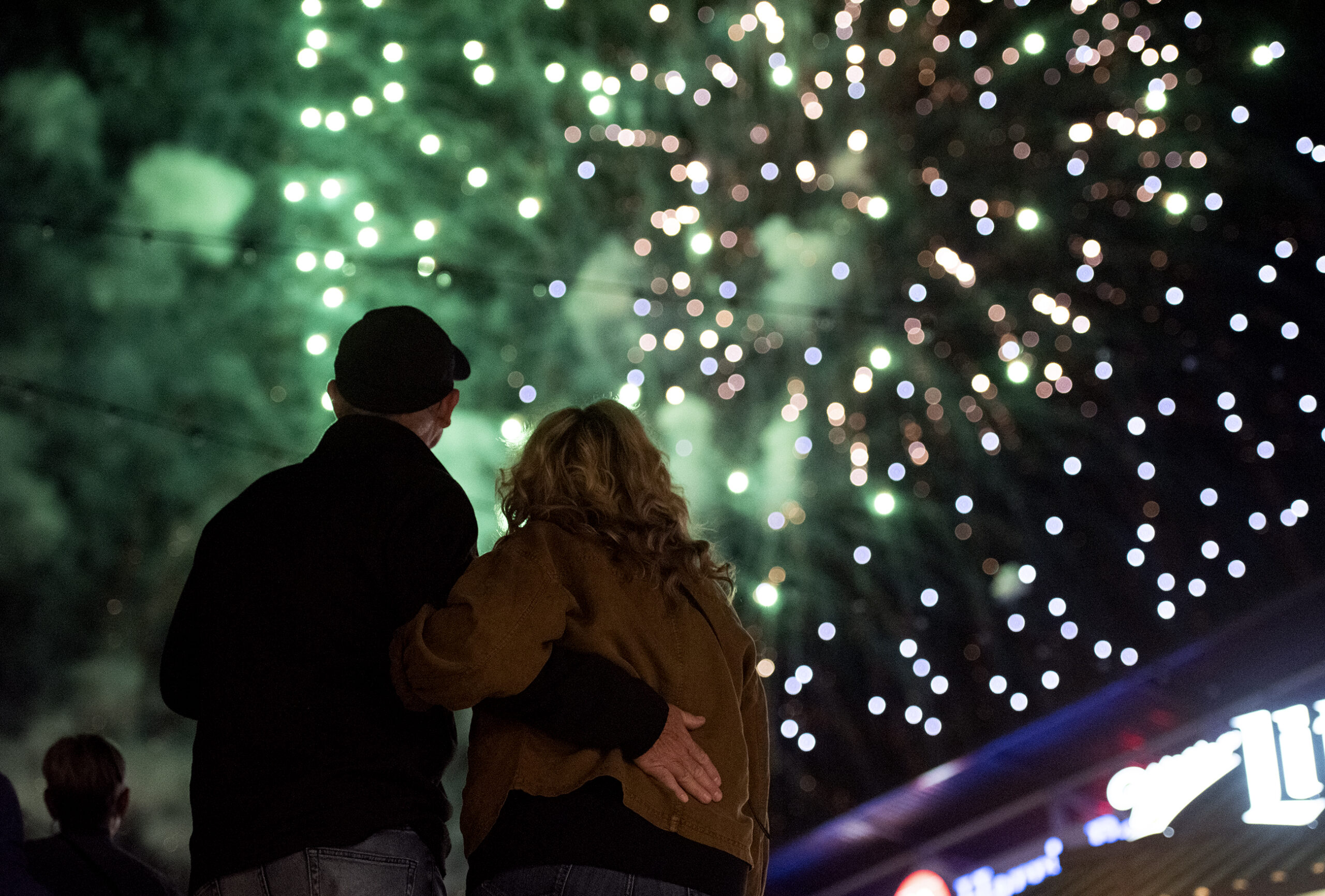 Green fireworks explode in the sky as a couple watches from the ground.
