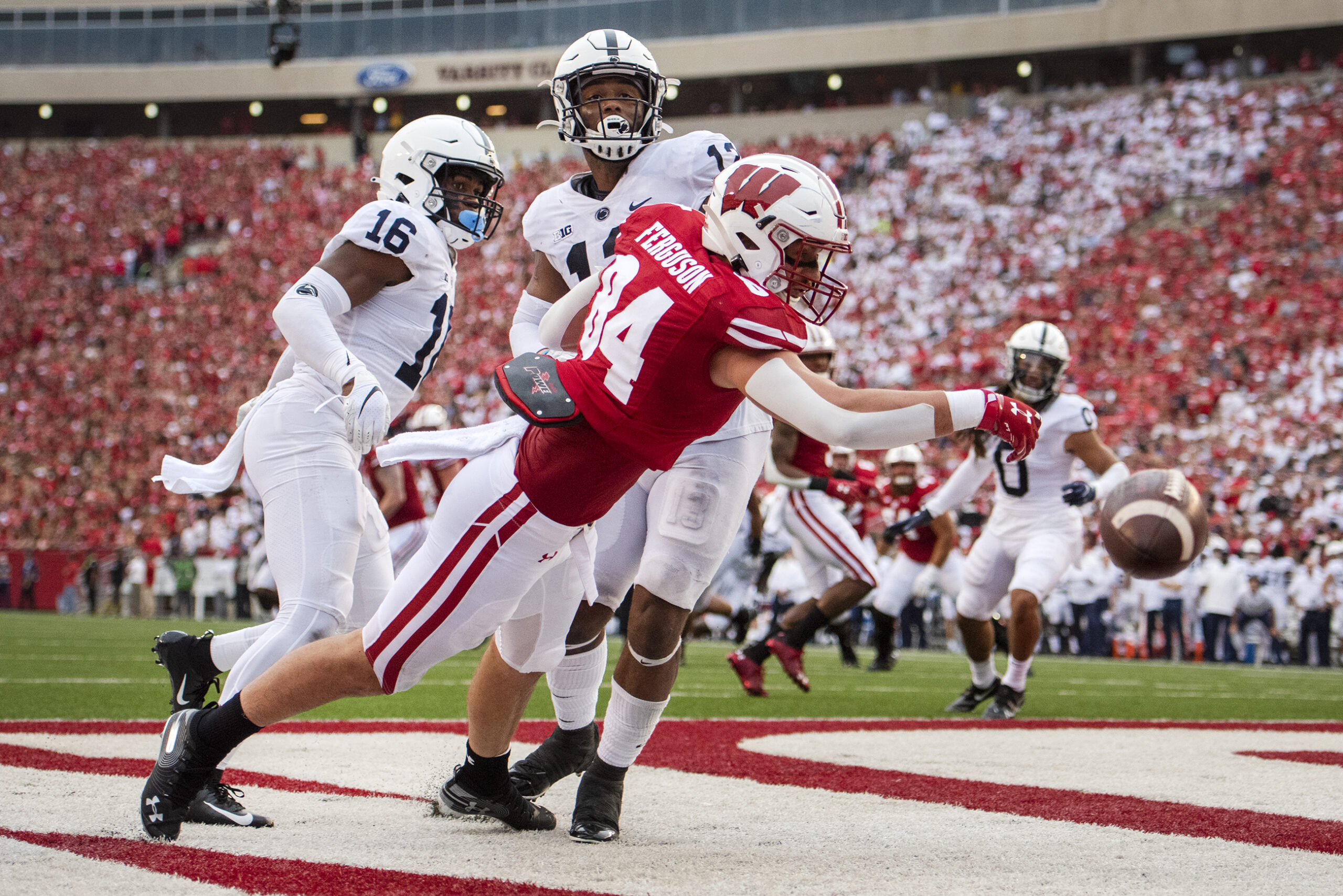 A Wisconsin player falls as he reaches for the ball. He's pushed by two Penn State defenders.