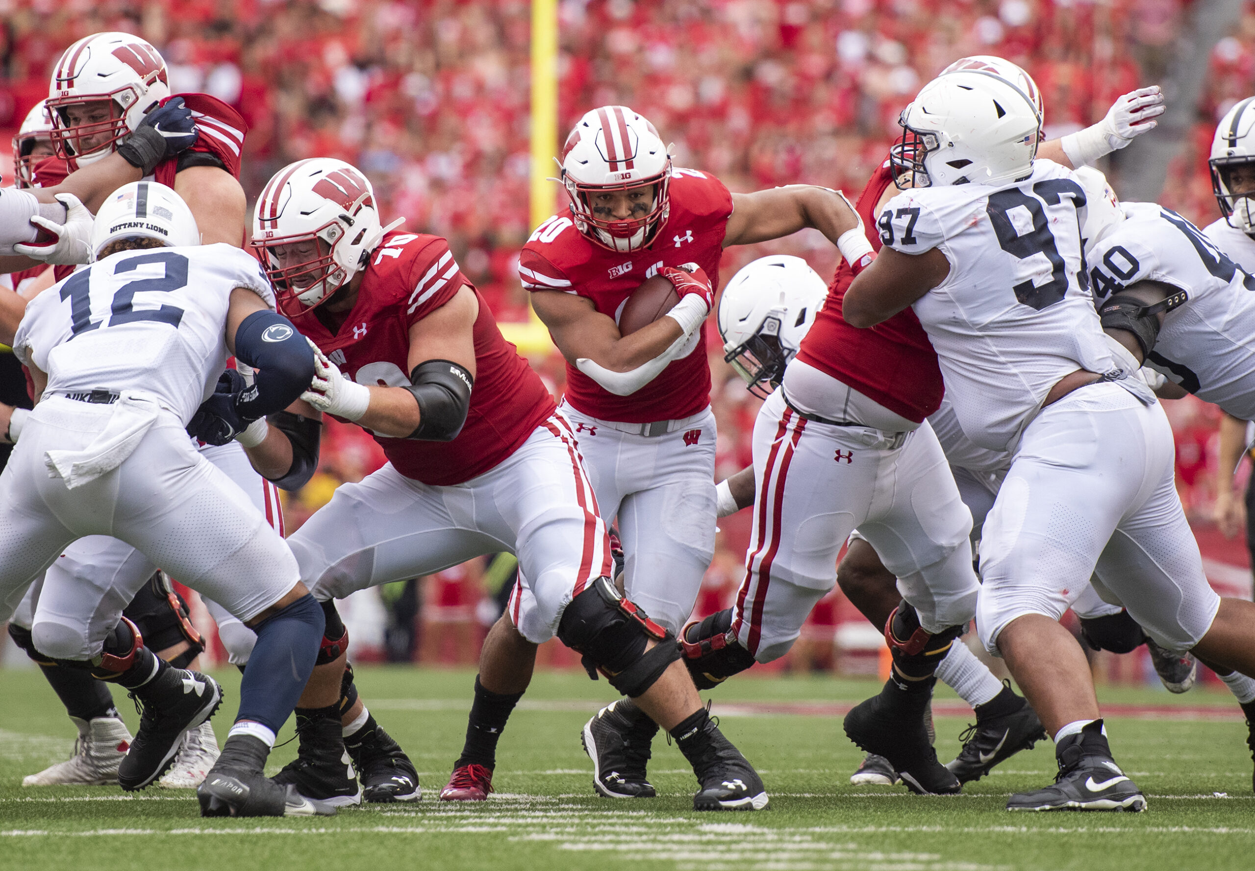 A Wisconsin player can be seen holding the ball securely and rushing through a hole in the Penn State defense.