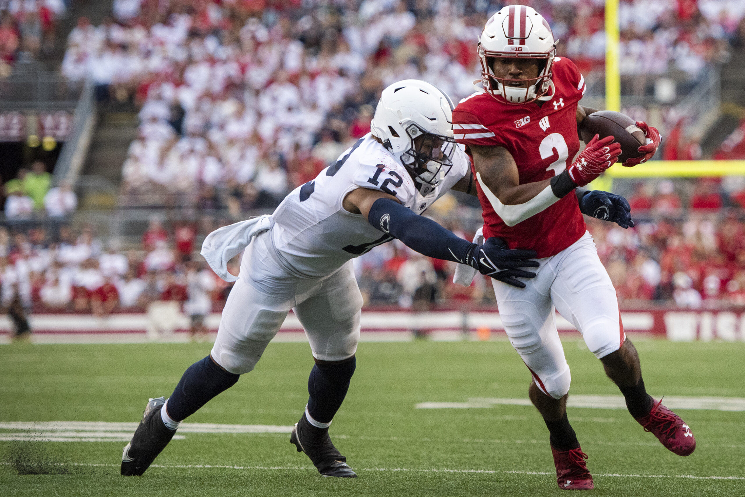 A Wisconsin player holds the ball and runs as a Penn State dives to tackle him.