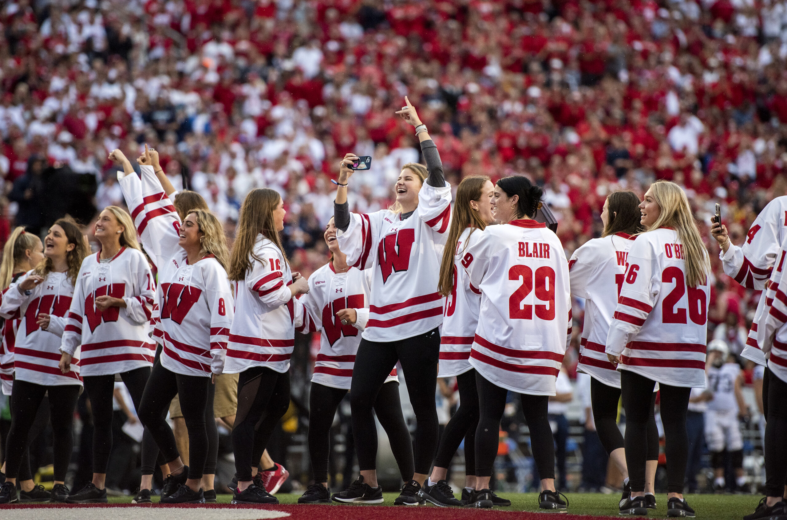 The Wisconsin women’s hockey team steps onto the field at Camp Randall as fans cheer.