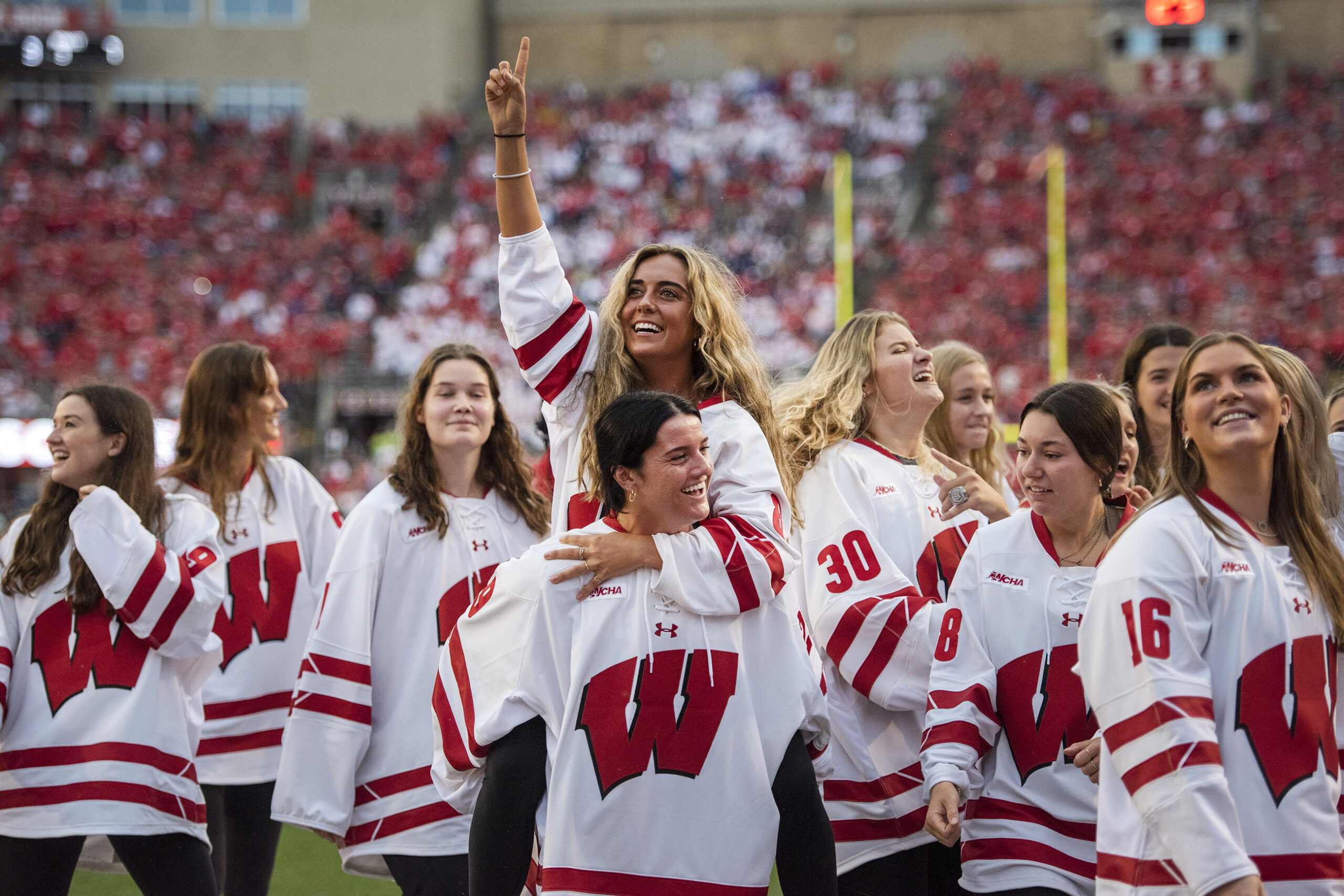The Wisconsin women’s hockey team steps onto the field at Camp Randall as fans cheer.