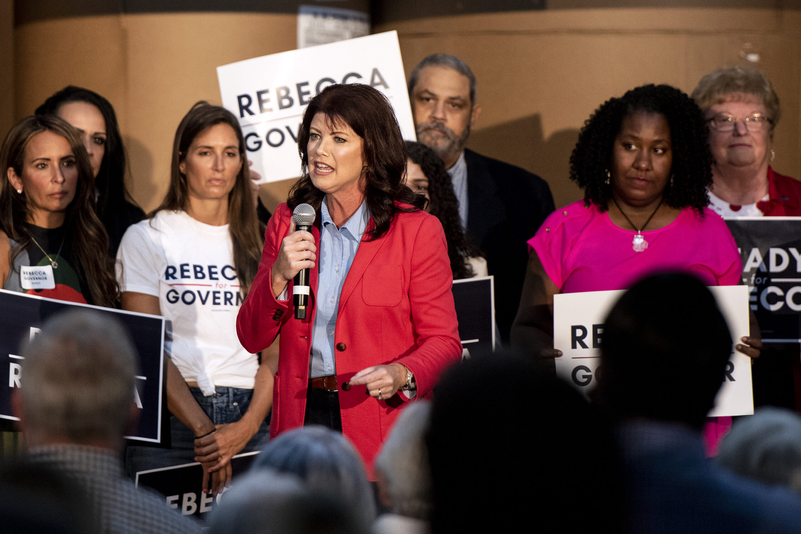 Rebecca Kleefisch speaks into a microphone while on stage with supporters holding campaign signs.