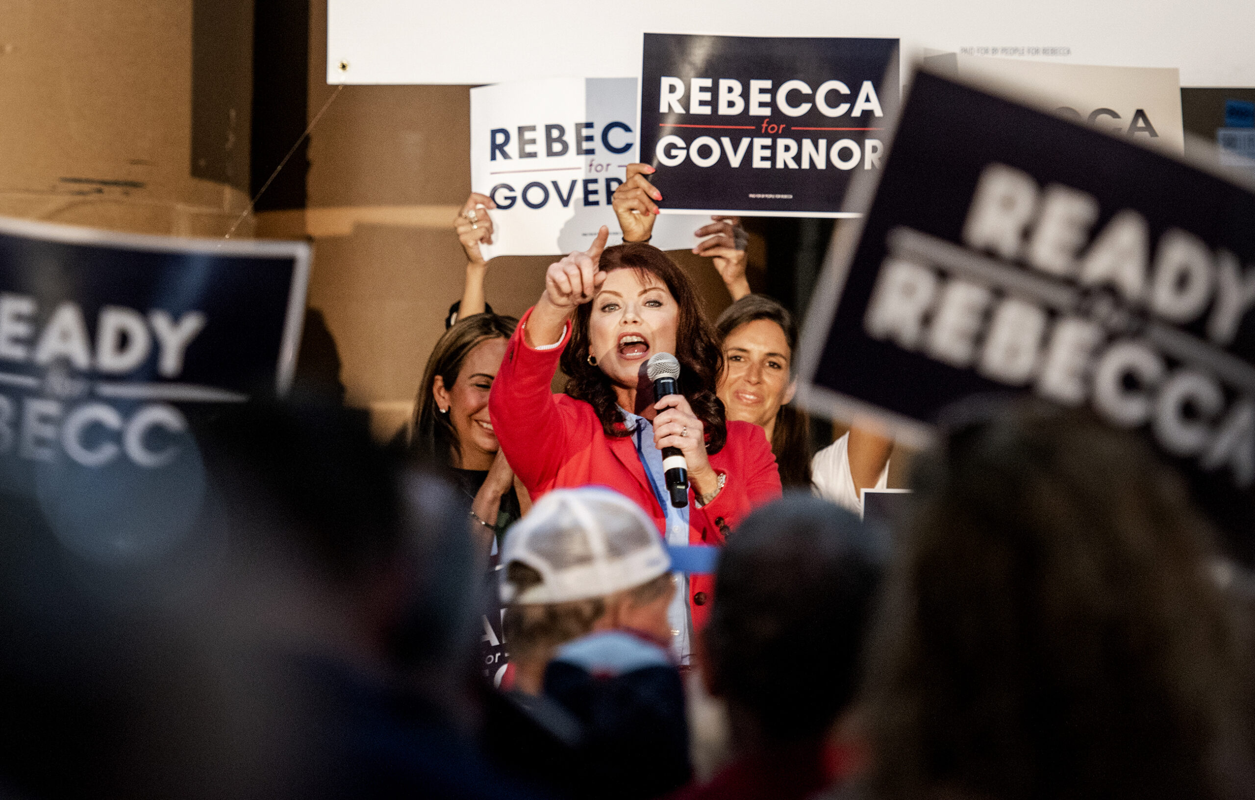 People in the crowd hold up campaign signs as Rebecca Kleefisch points to them while speaking into a microphone.