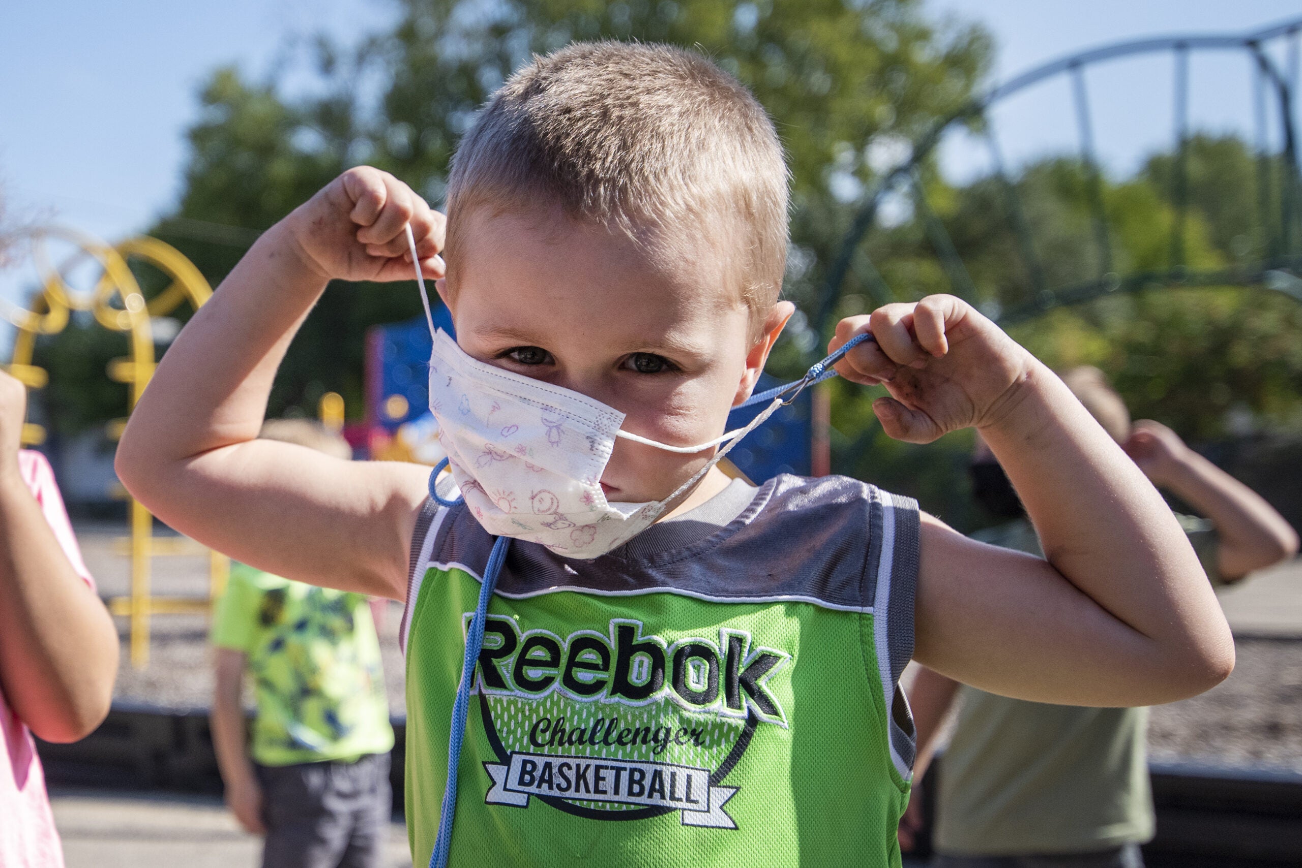 A student pulls up the ear strings of a face mask to his face before entering the school building.