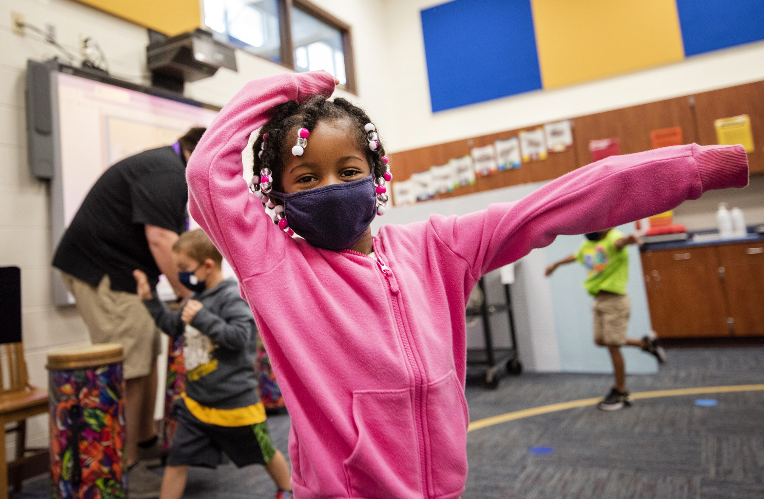 A girl in a pink jacket wears a face mask as she dances in class.