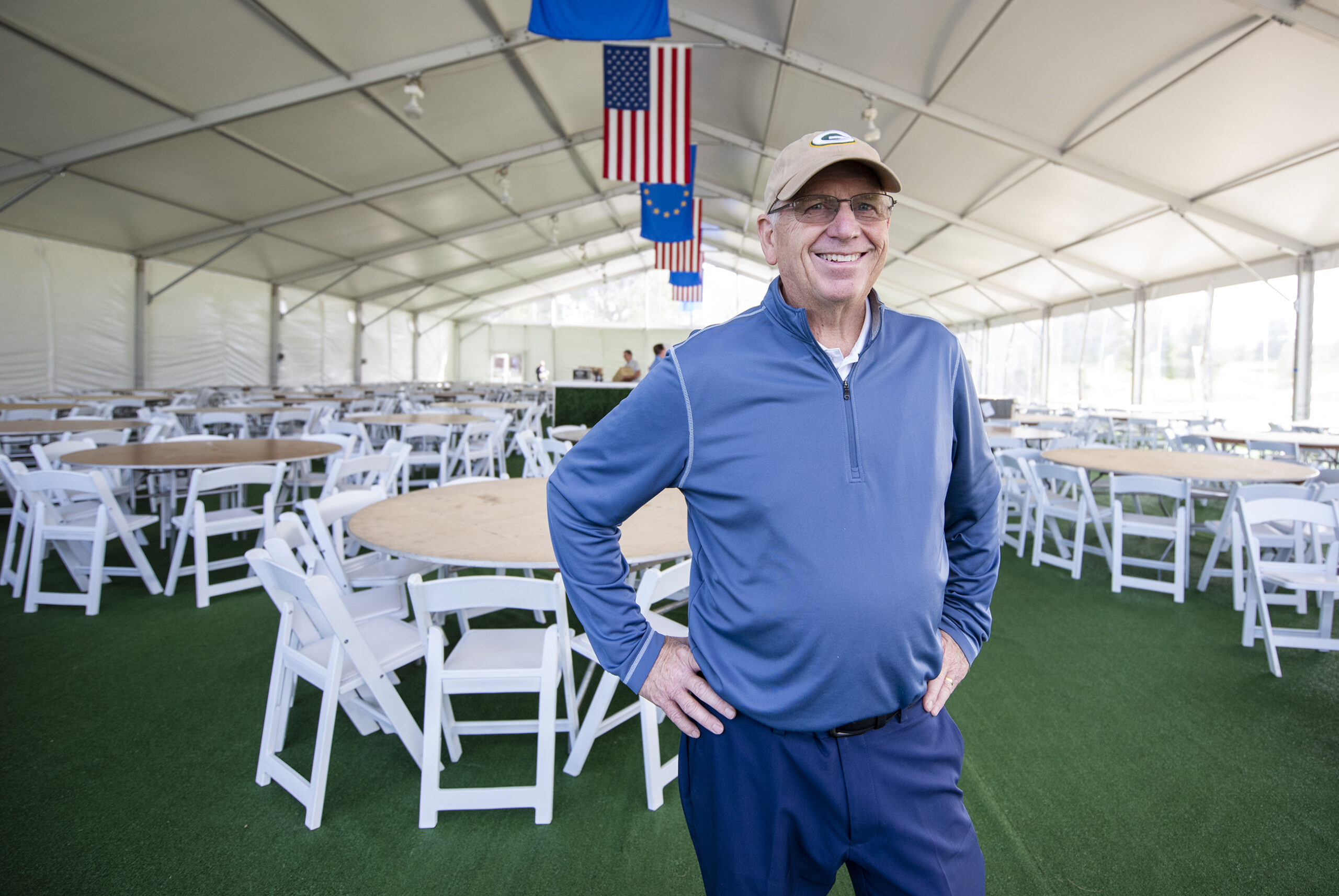 A man stands inside of a large tent with several circular dining tables inside.