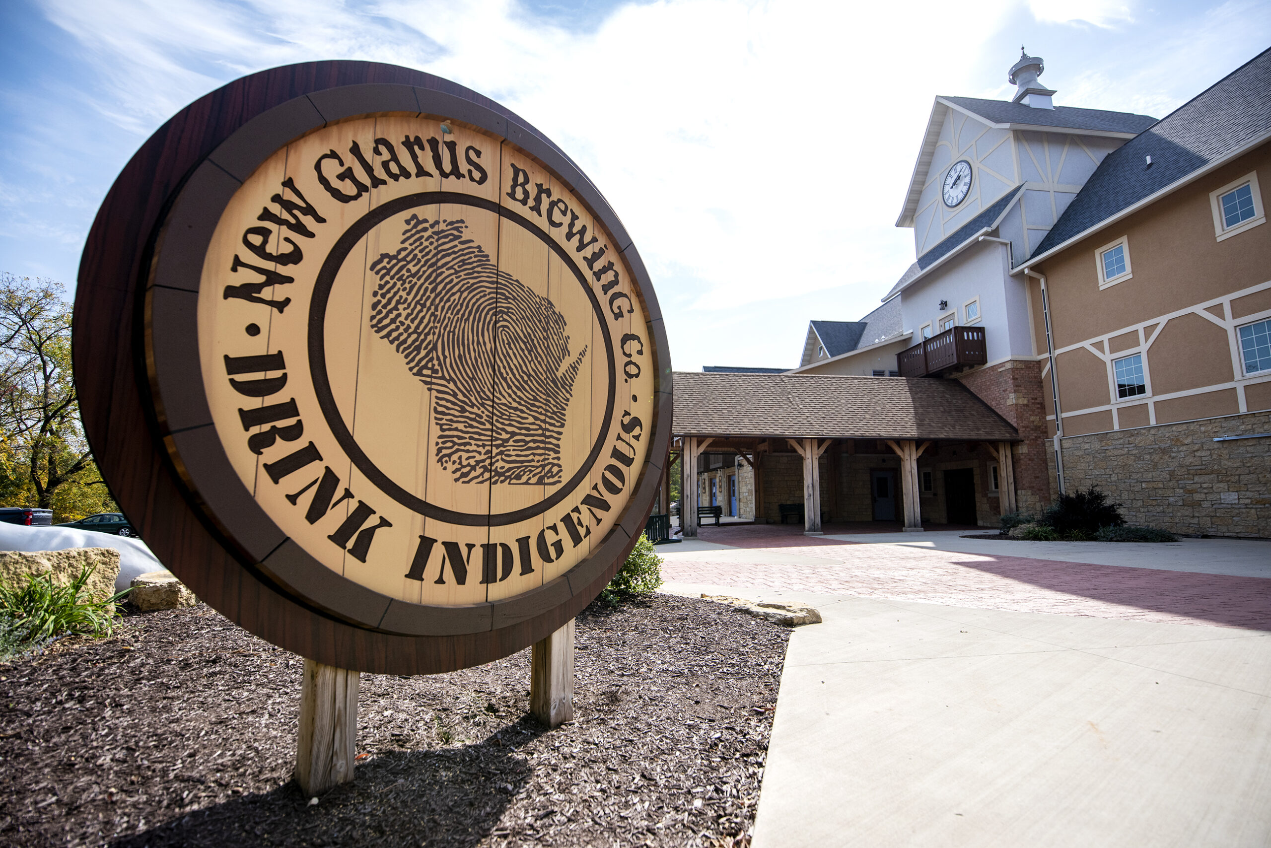 A sign says "New Glarus Brewing Co., Drink Indigenous" outside of the brewery.