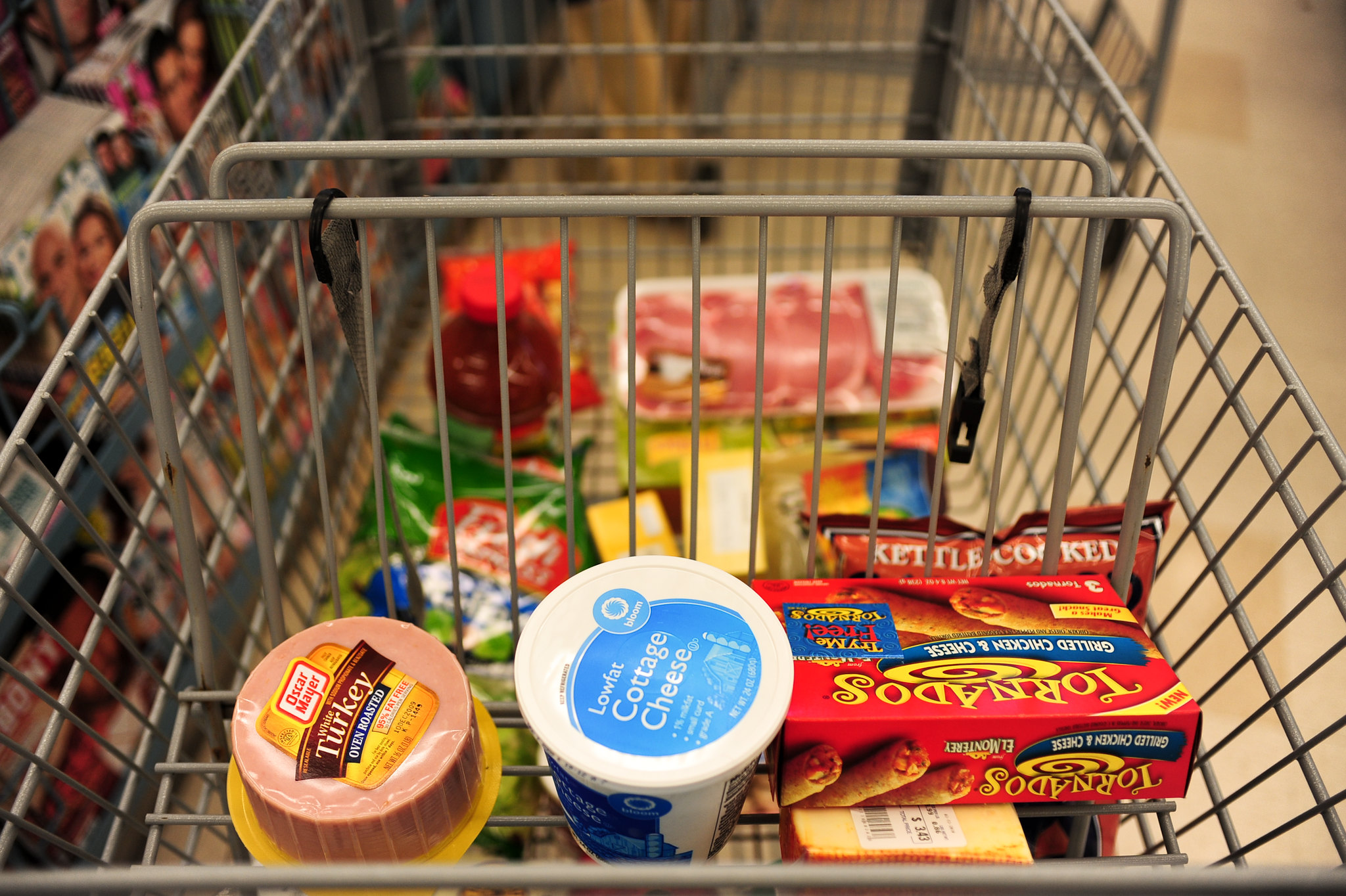 A close-up view of a shopping cart in a grocery store with a few items in the cart.