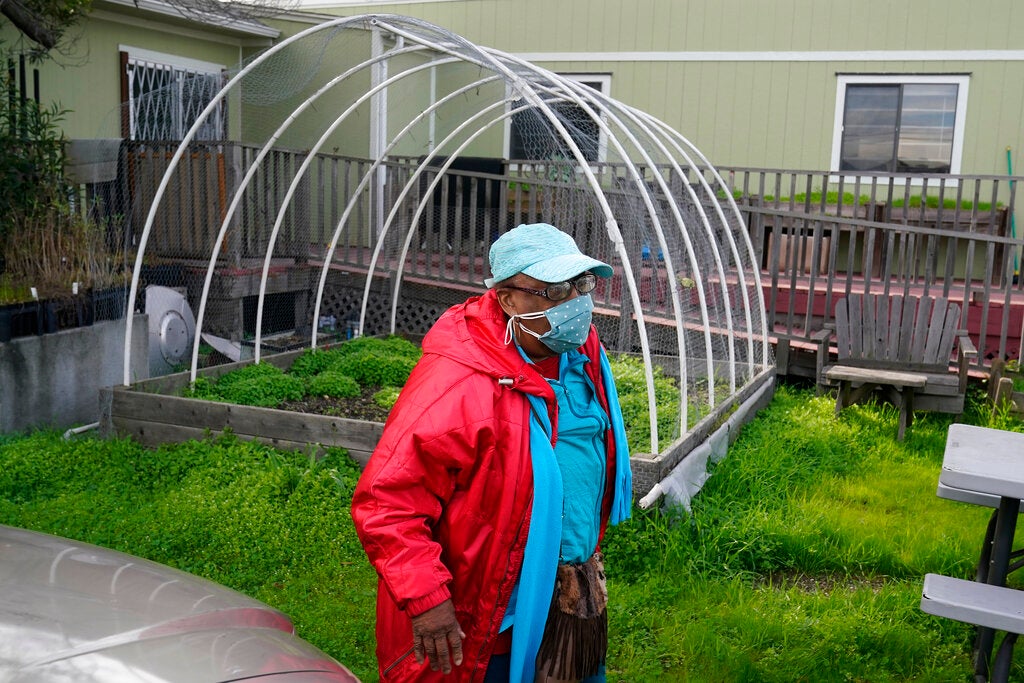A black woman wearing a mask is outside near the metal bars of a hoop house stand.