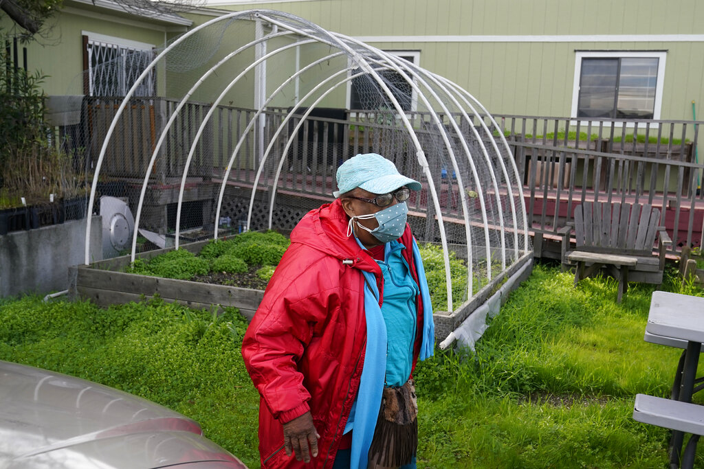 A black woman wearing a mask is outside near the metal bars of a hoop house stand.